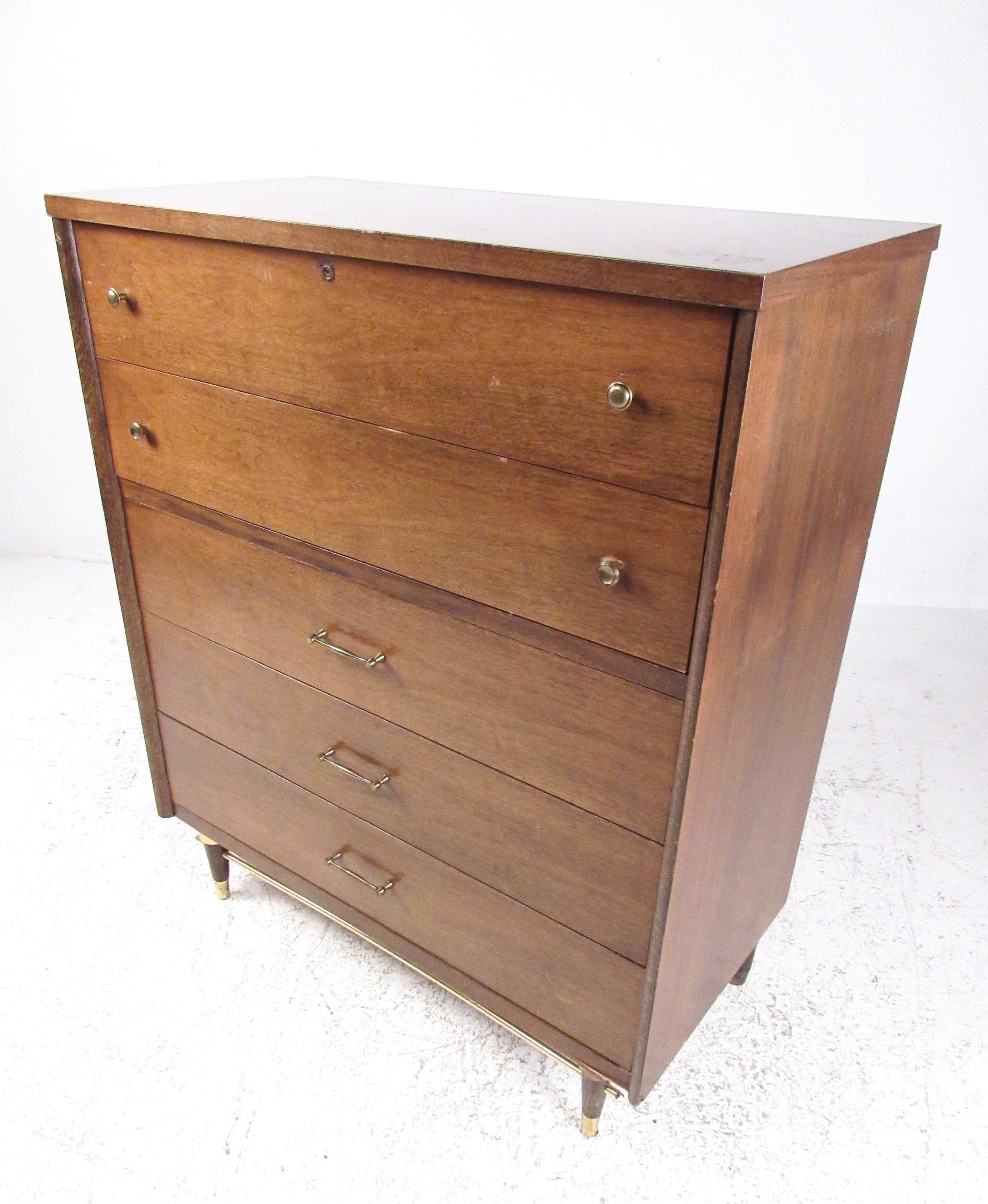 This vintage modern five-drawer highboy dresser features unique Mid-Century Modern design including walnut finish with brass details. Rounded drawer pulls and tapered legs add to the unique mid-mod appeal of this tall bedroom dresser. Please confirm