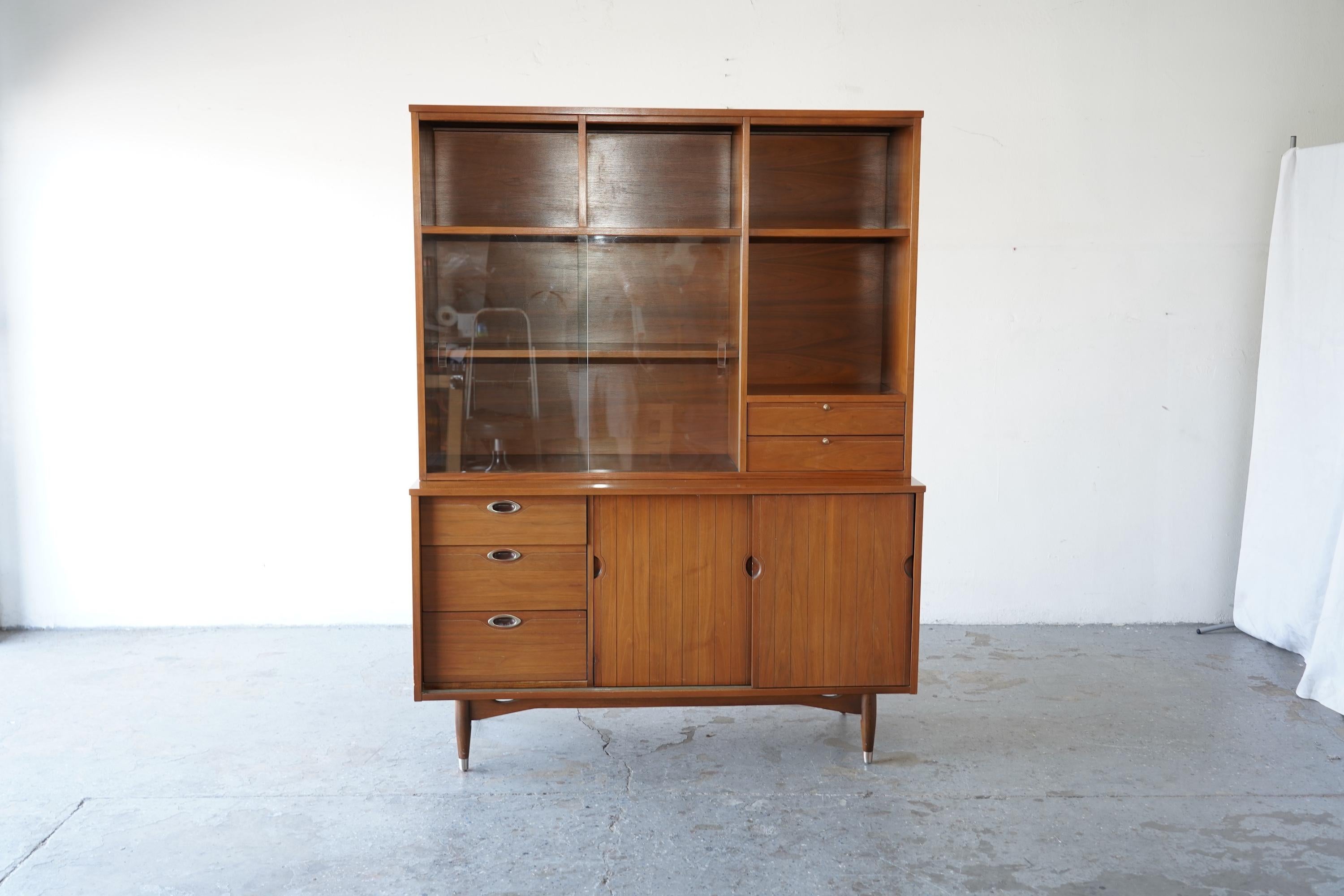 A versatile mid-century modern two-piece hutch and credenza by Hooker Furniture Mainline Collection, crafted  circa 1960s. This piece showcases clean lines, walnut veneers, and iconic details including sculpted oval pulls, sliding tambour doors, and