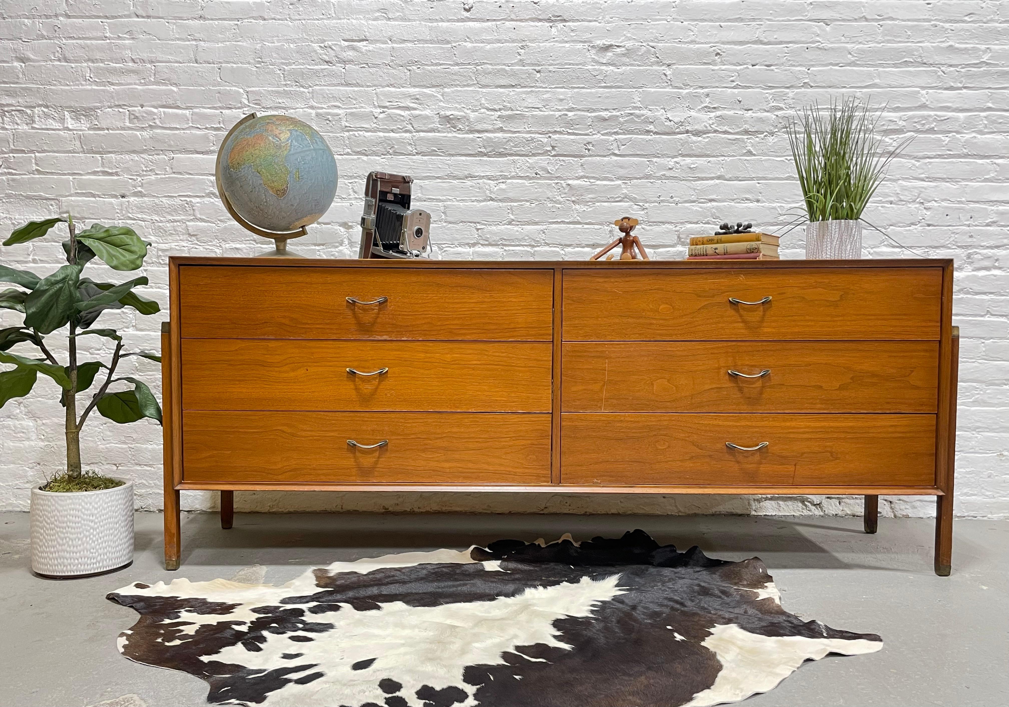 Mid Century Modern Walnut Long Dresser / Credenza in the style of Dunbar, c. 1960’s.  This long credenza is highlighted by legs that are attached along the sides, giving the credenza a floating appearance. The legs are topped and capped with brass