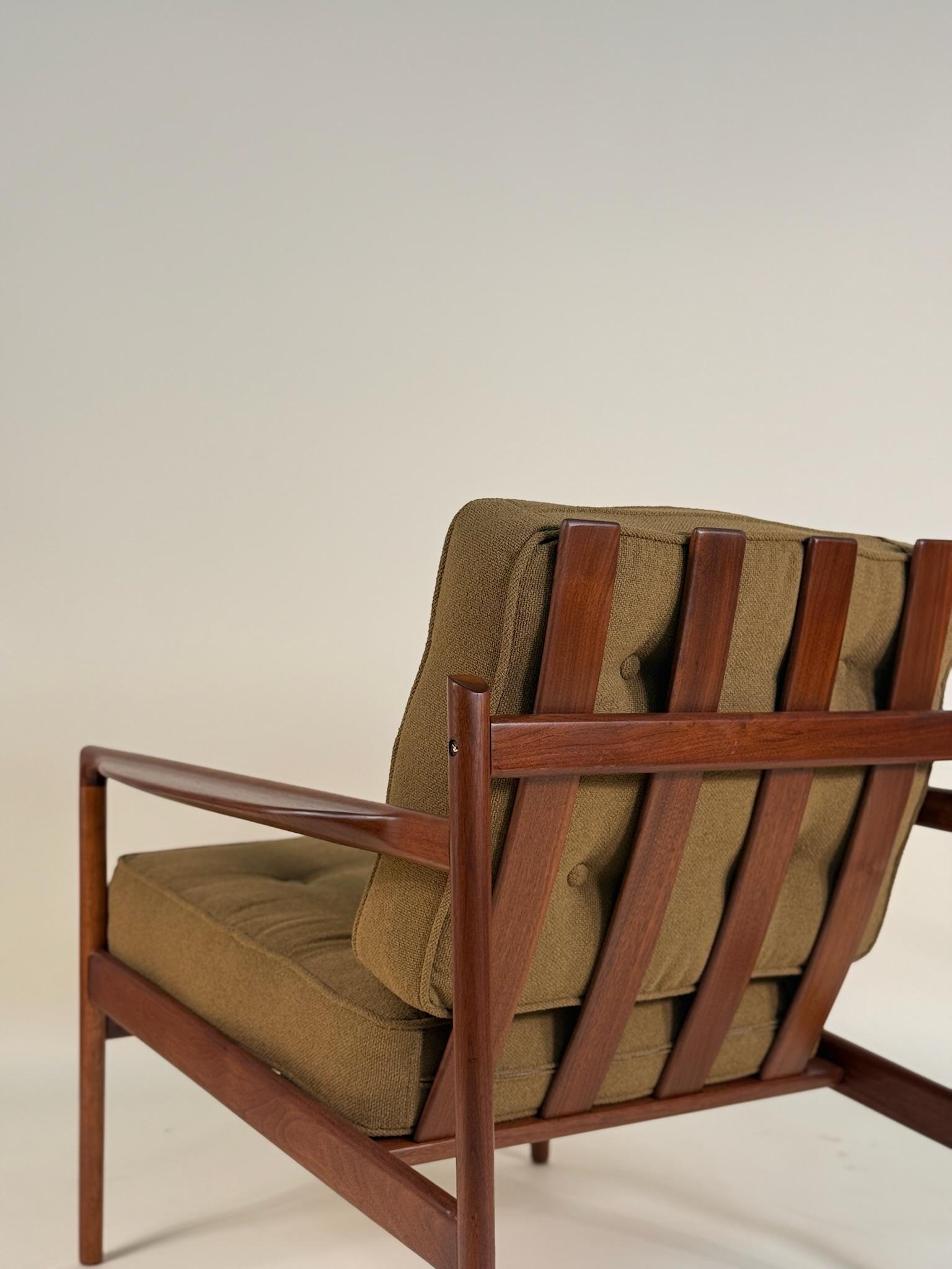 Impresionante tumbona diseñada por Ib Kofod-Larsen y fabricada en Dinamarca hacia la década de 1960. Este distintivo diseño moderno danés presenta una sólida estructura de madera de nogal con cuatro grandes listones que actúan como respaldo, además