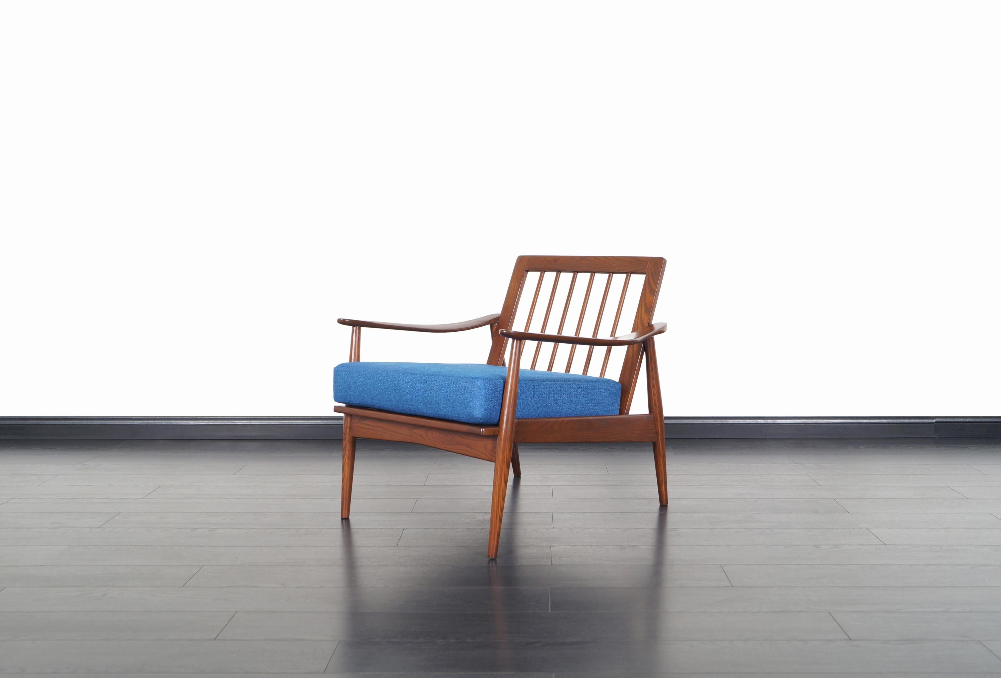 Fabulous Mid-Century Modern lounge chair manufactured in the United States. This chair features a solid walnut-stained oak frame with sculptural armrests and a slatted backrest. The perfectly symmetrical proportions and clean lines on this design