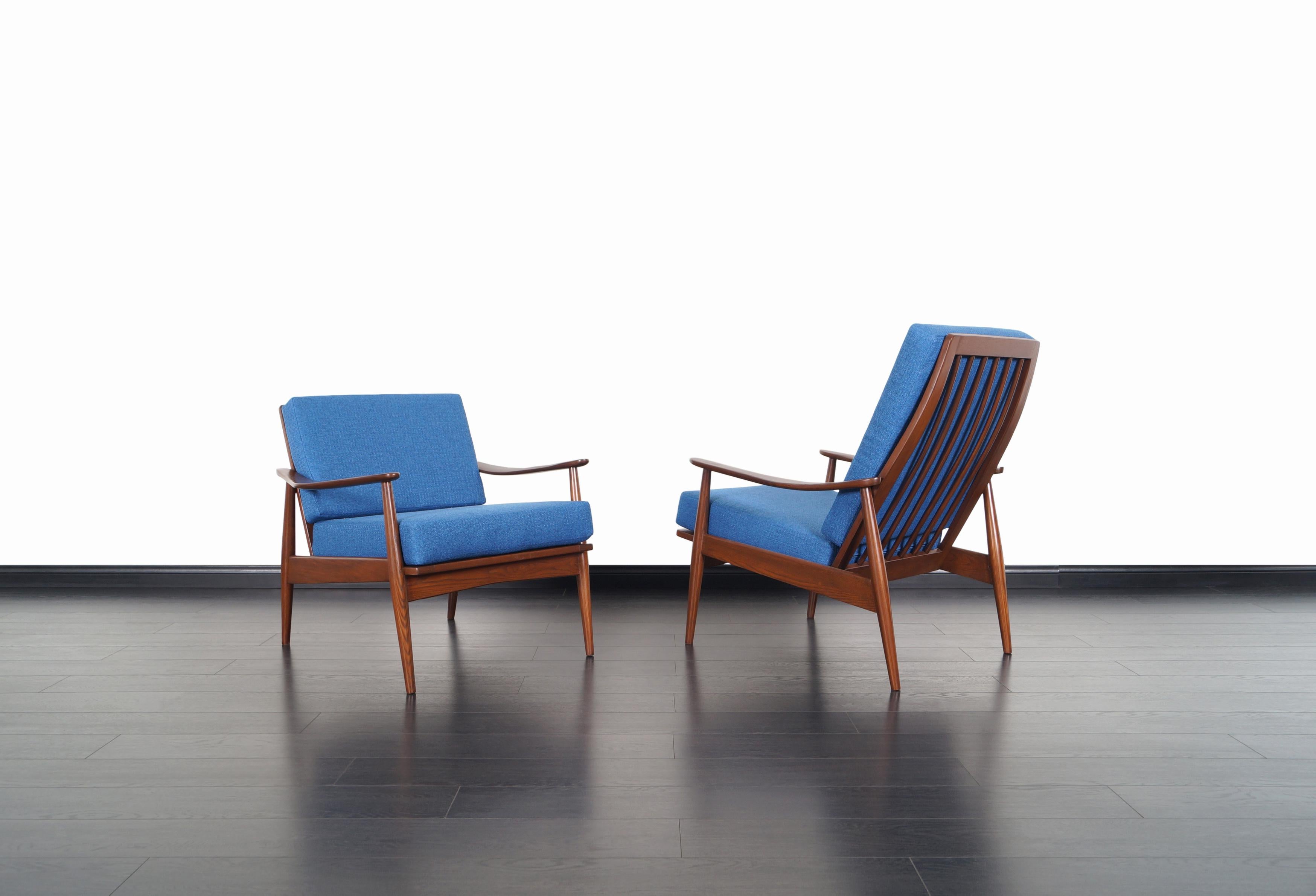 Fabulous pair of Mid-Century Modern lounge chairs, manufactured in the United States, circa 1950s. These chairs features a solid walnut stained oak frames with sculptural armrests and slatted backrests. The perfectly symmetrical proportions and
