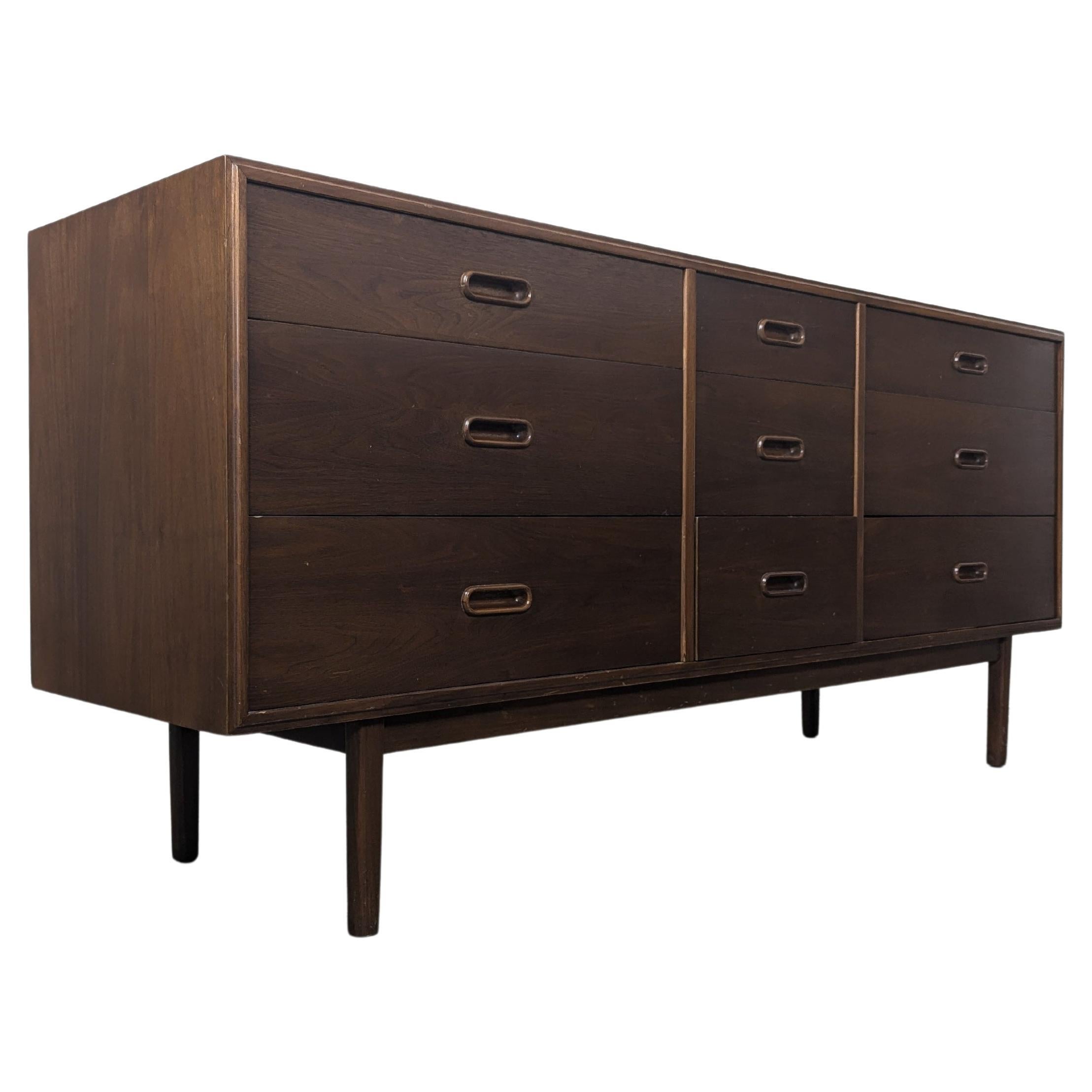 For sale is a stunning vintage mid-century modern walnut nine-drawer dresser designed by the renowned Jack Cartwright for Founders, circa 1960s. This exquisite piece measures approximately 67” wide, 18” deep, and 30.25” tall, offering ample storage