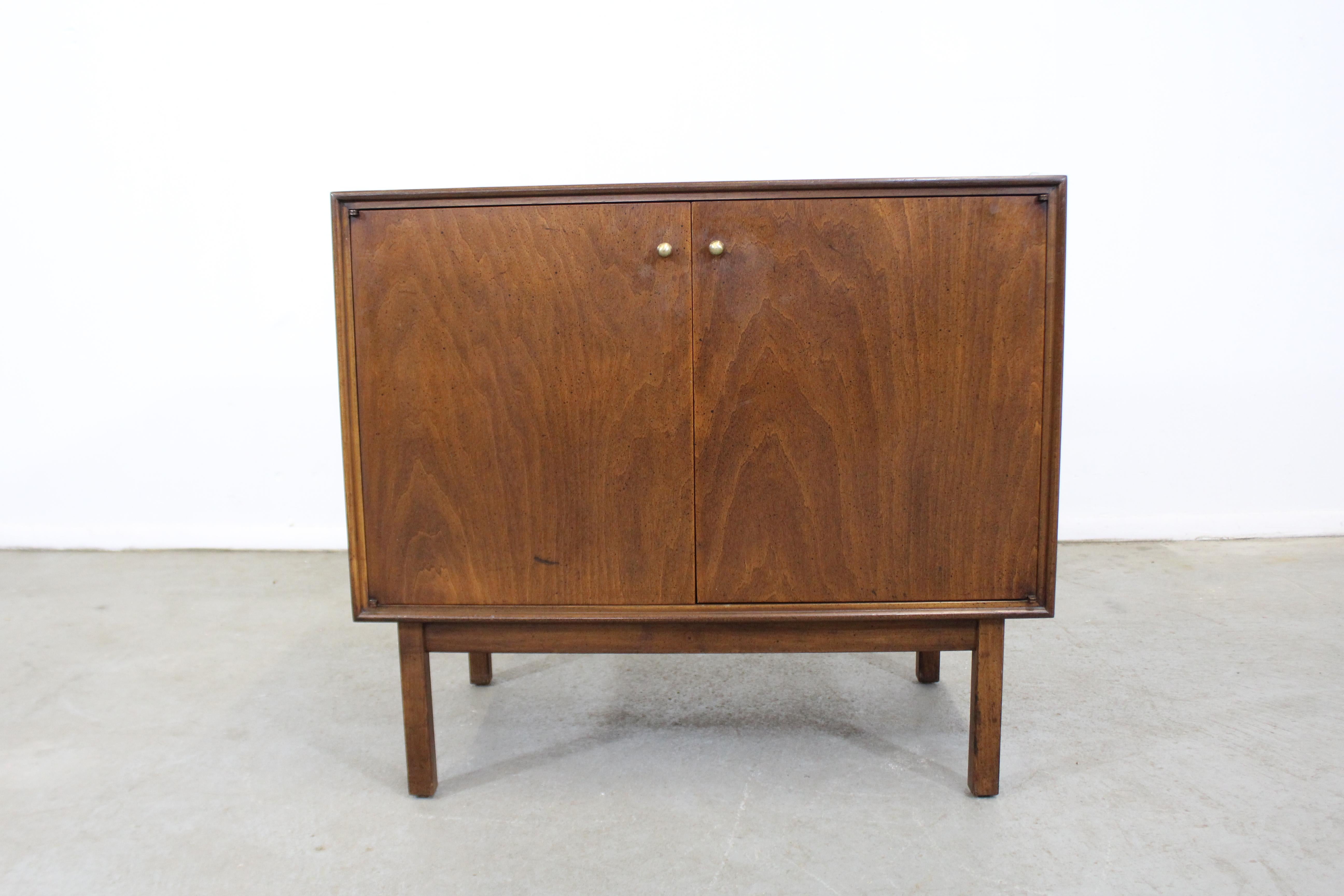 What a find. Offered is a gorgeous Mid-Century Modern mini credenza or server. It is made of walnut with brass pulls, featuring two doors and adjustable inner shelving. It is in very good condition for its age showing slight surface wear and