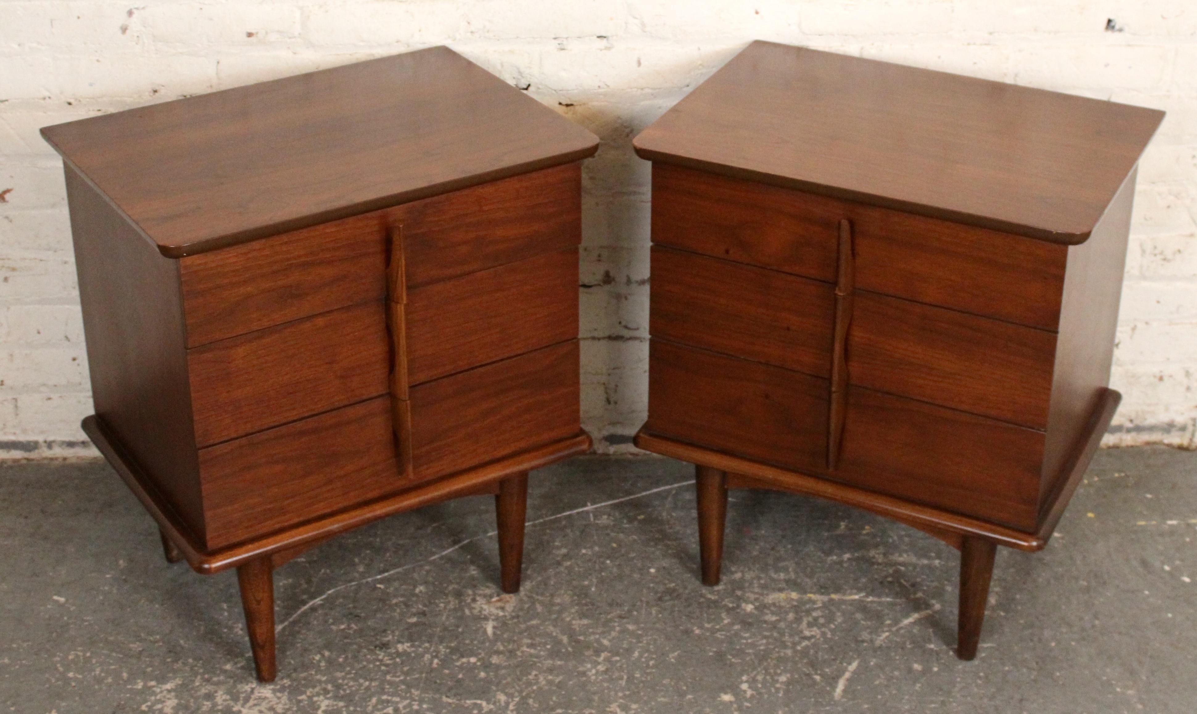 Magnifiquement fabriquée en noyer riche, cette paire de tables de nuit de style moderne du milieu du siècle par United Furniture présente des lignes épurées, des poignées intégrées sculptées et des pieds effilés légèrement évasés typiques de