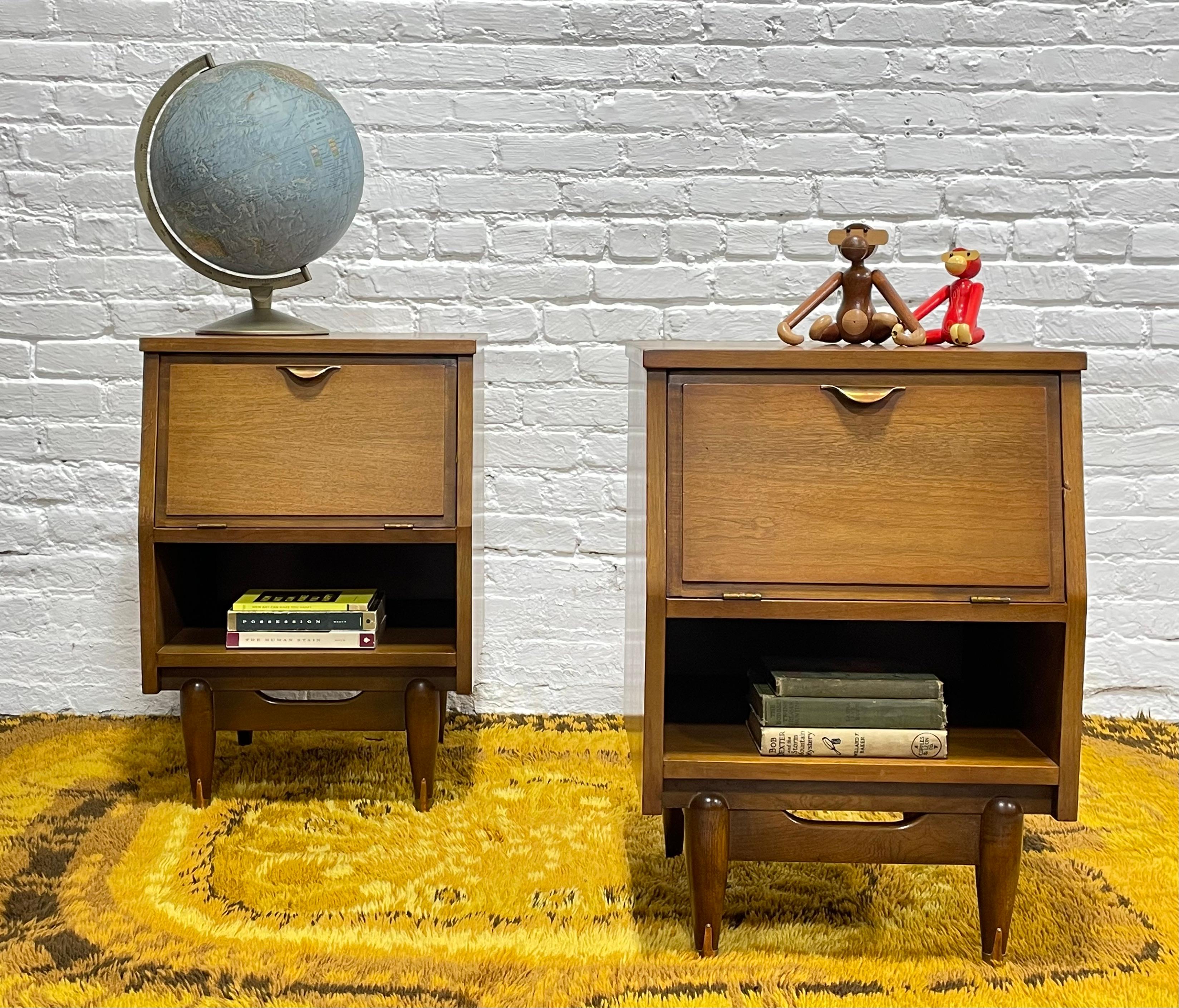 Mid Century Modern Walnut Nightstands by Hooker Mainline, c. 1960’s.  The nightstands feature drop down doors, perfect for setting down your morning coffee and breakfast upon while still retaining the tabletop space. There is plenty of storage space