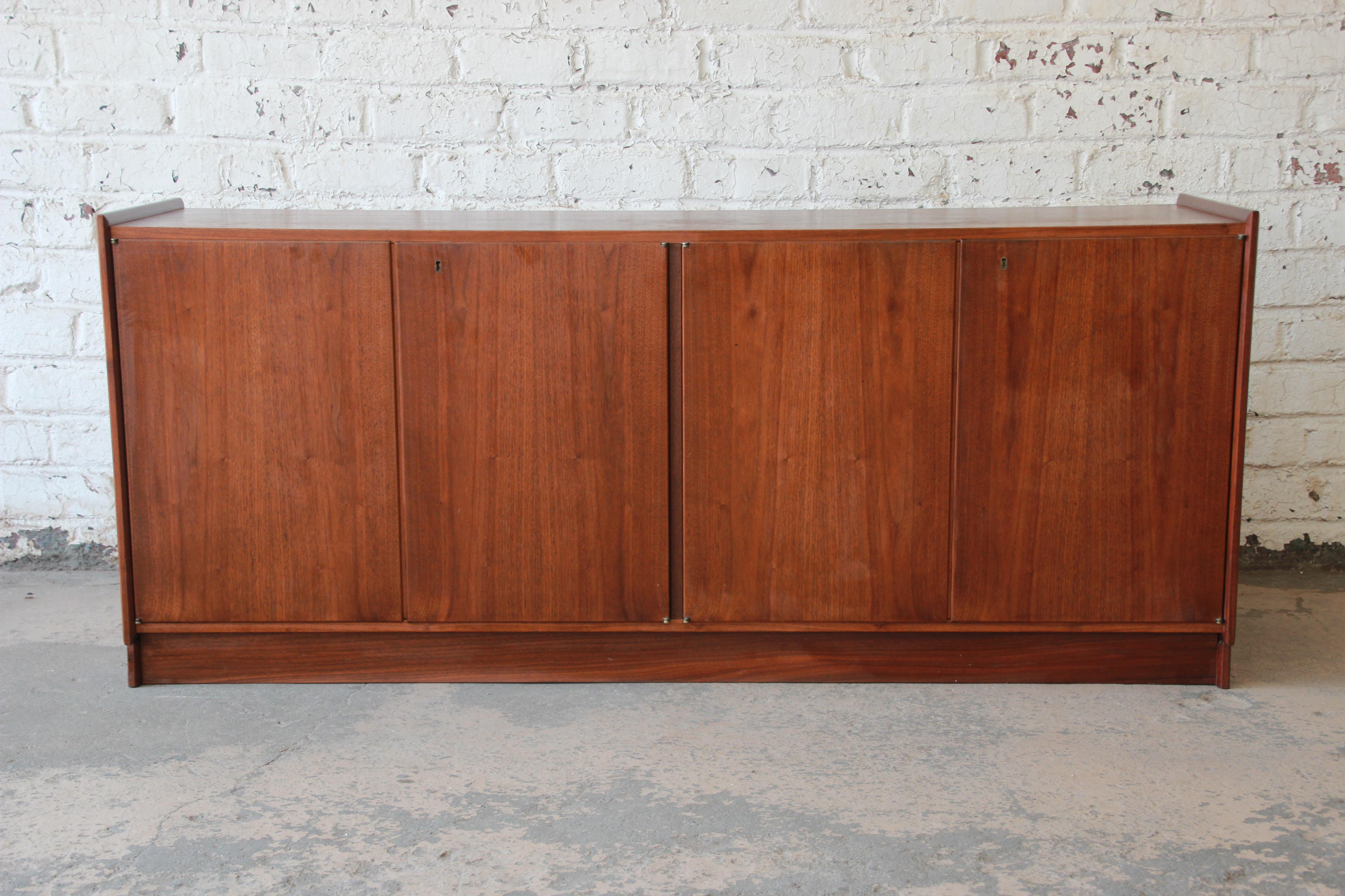 A very nice Mid-Century Modern walnut record cabinet. The cabinet features gorgeous walnut wood grain and sleek mid-century design. It offers ample room for storage. It has record slots, an adjustable shelf, and a slide-out shelf for a record player