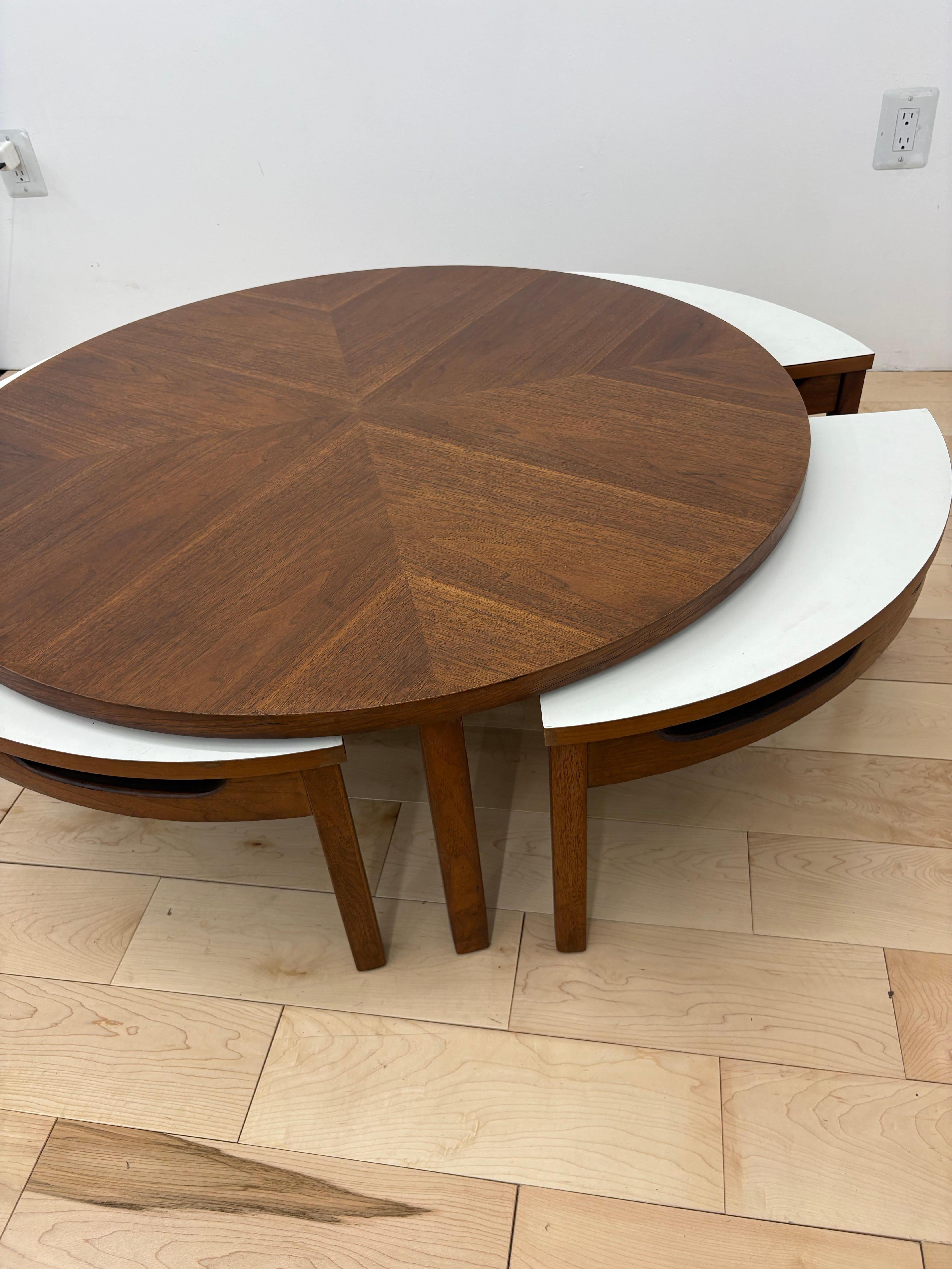 A rare and sculpturally refined mid-century modern round walnut coffee table with four integrated white laminate and walnut pie-wedge nesting tables, dating to the 1960s. This modular five-piece set is a masterclass in both form and function,