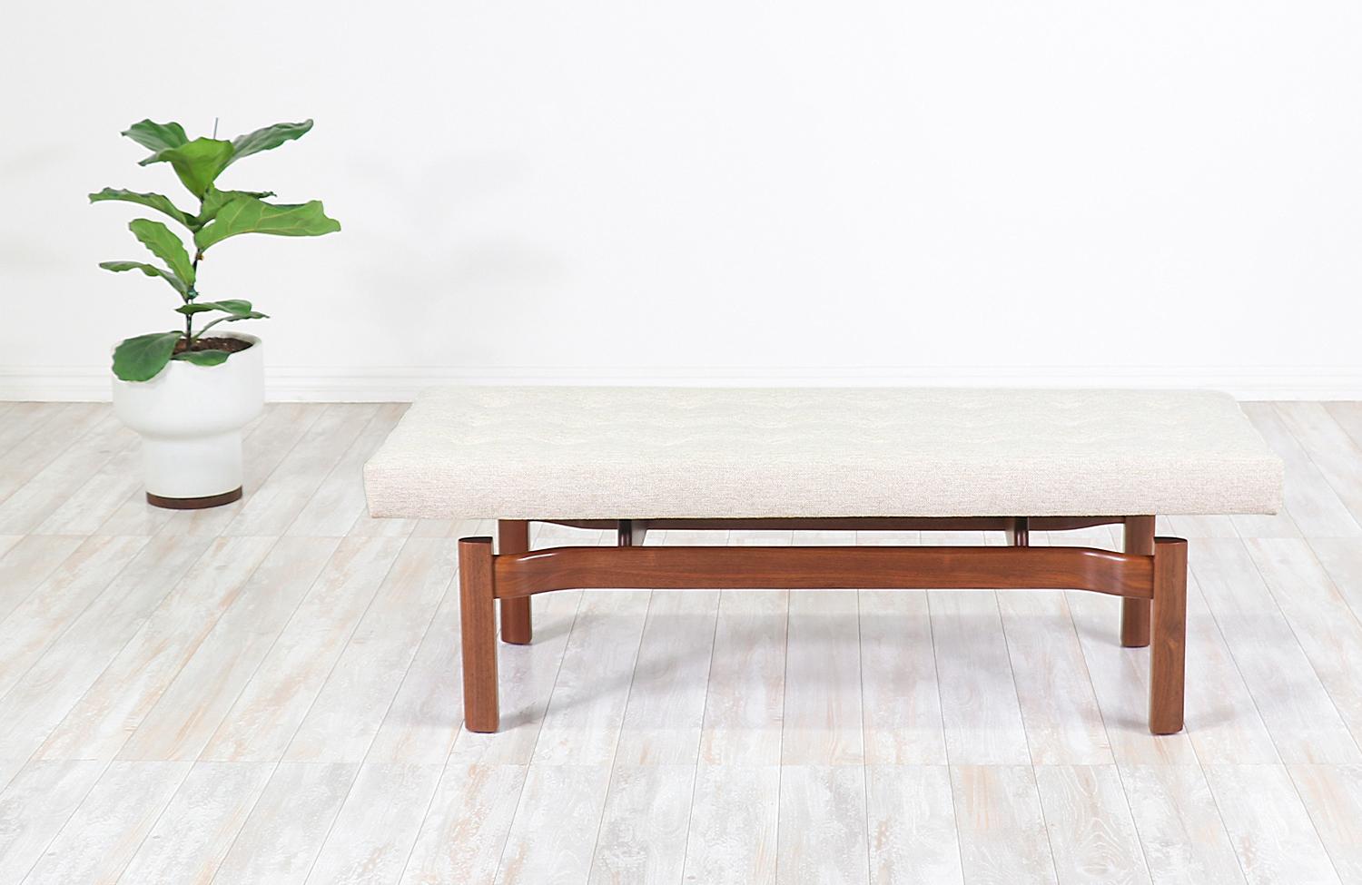 Sculpted Mid-Century Modern bench designed and manufactured in the United States, circa 1950s. This elegantly carved bench features a solid walnut wood base with a long cushion held by two perpendicular stretchers in a way that makes it seem like a