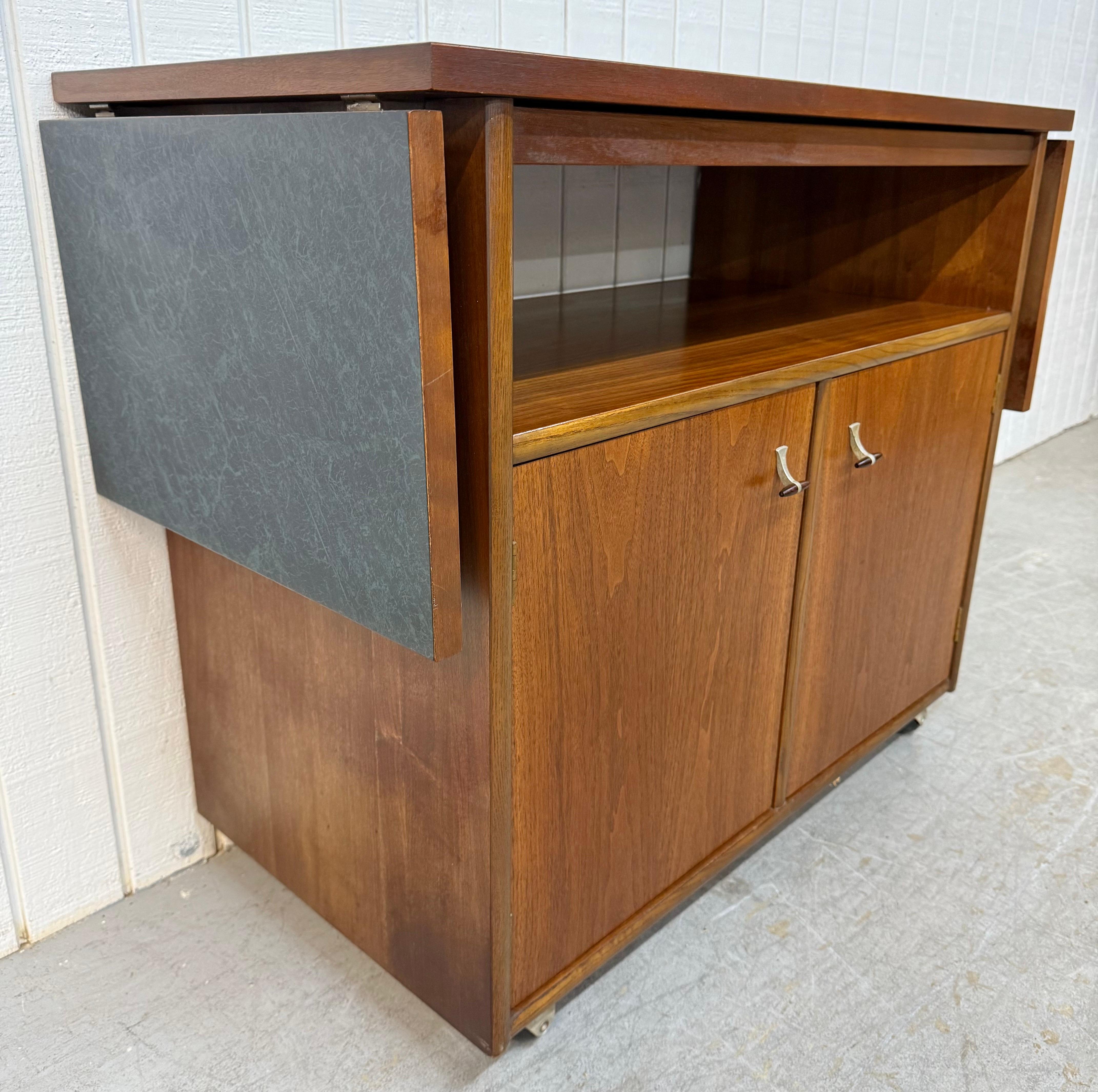 Questo annuncio si riferisce a un carrello da portata in legno di noce di epoca moderna. Il design è lineare, il piano a ribalta laminato si espande fino a una lunghezza di 60,25