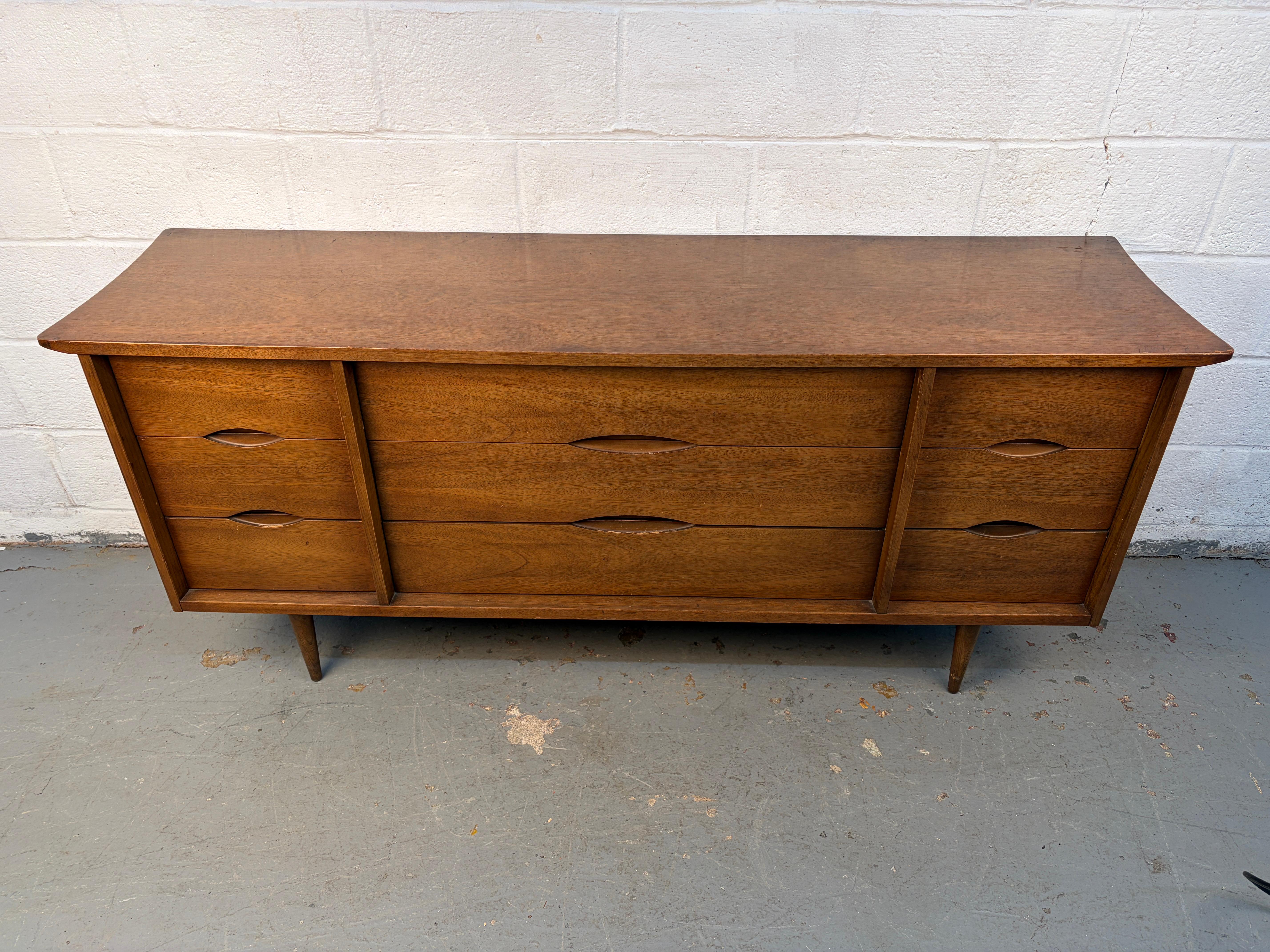 Una credenza in noce di metà secolo, splendidamente realizzata da Bassett Furniture Inc. dell'Indiana. Caratterizzato da linee pulite, ricche venature del legno e un ampio spazio di archiviazione, questo pezzo riflette la qualità costruttiva del