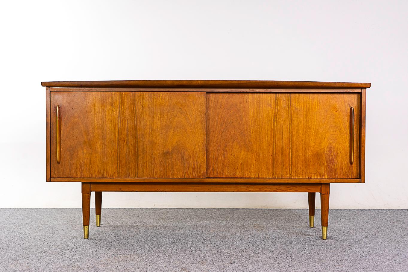 Walnut mid-century sideboard by Deilcraft, circa 1960's. Solid overhanging curved edges, sleek handles with metal inlay and tapering capped legs! Sliding doors open to a slim cutlery drawer and 2 fixed height shelves. As is condition, minor wear and