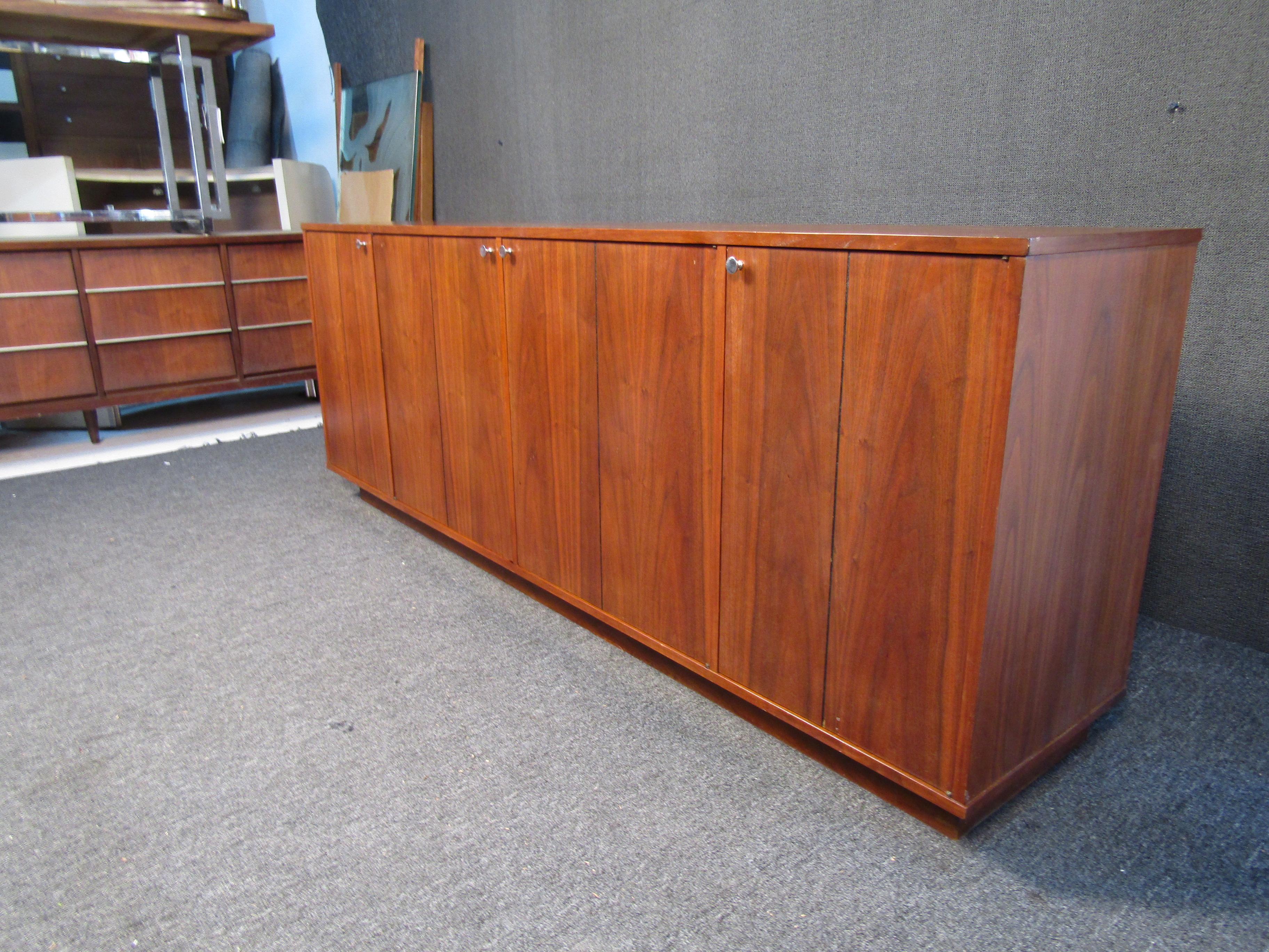 This impressive walnut sideboard offers plenty of storage space and slide-out shelves to aid in organization, all in a well-crafted Mid-Century Modern design. Metal knobs accent a clean woodgrain exterior. Please confirm item location with seller