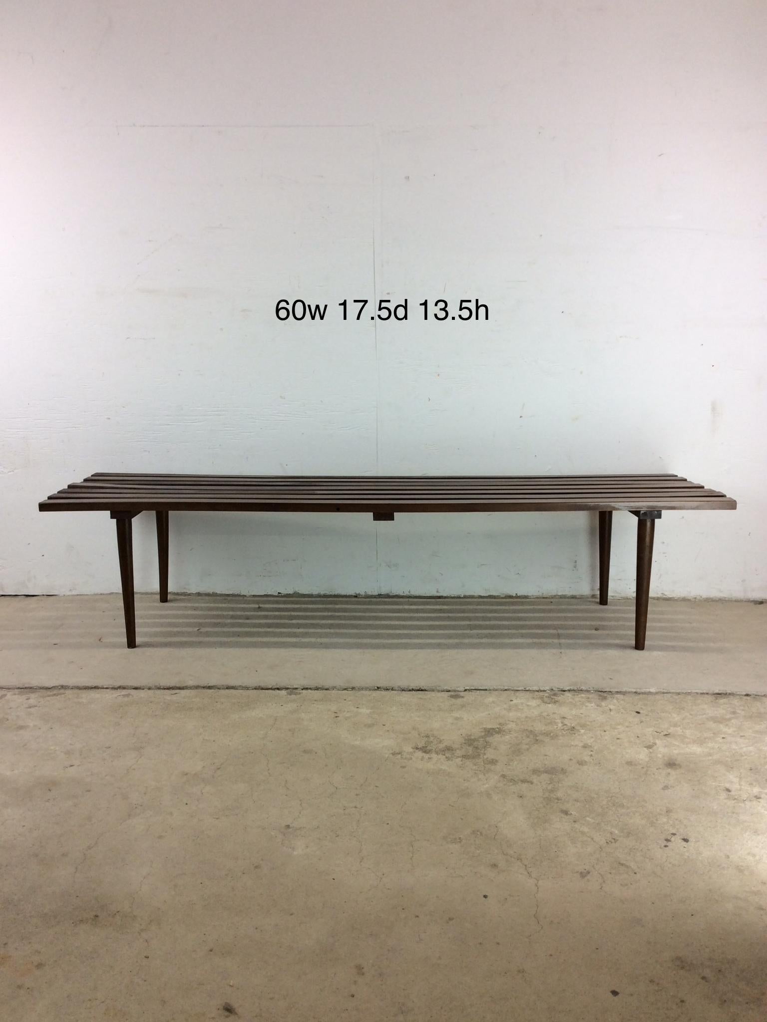 Ce banc à lattes / table basse moderne du milieu du siècle présente une construction en bois dur, une finition en noyer d'origine et de grands pieds effilés. Contrairement à beaucoup de ces bancs à lattes sur le marché, celui-ci est estampillé Made