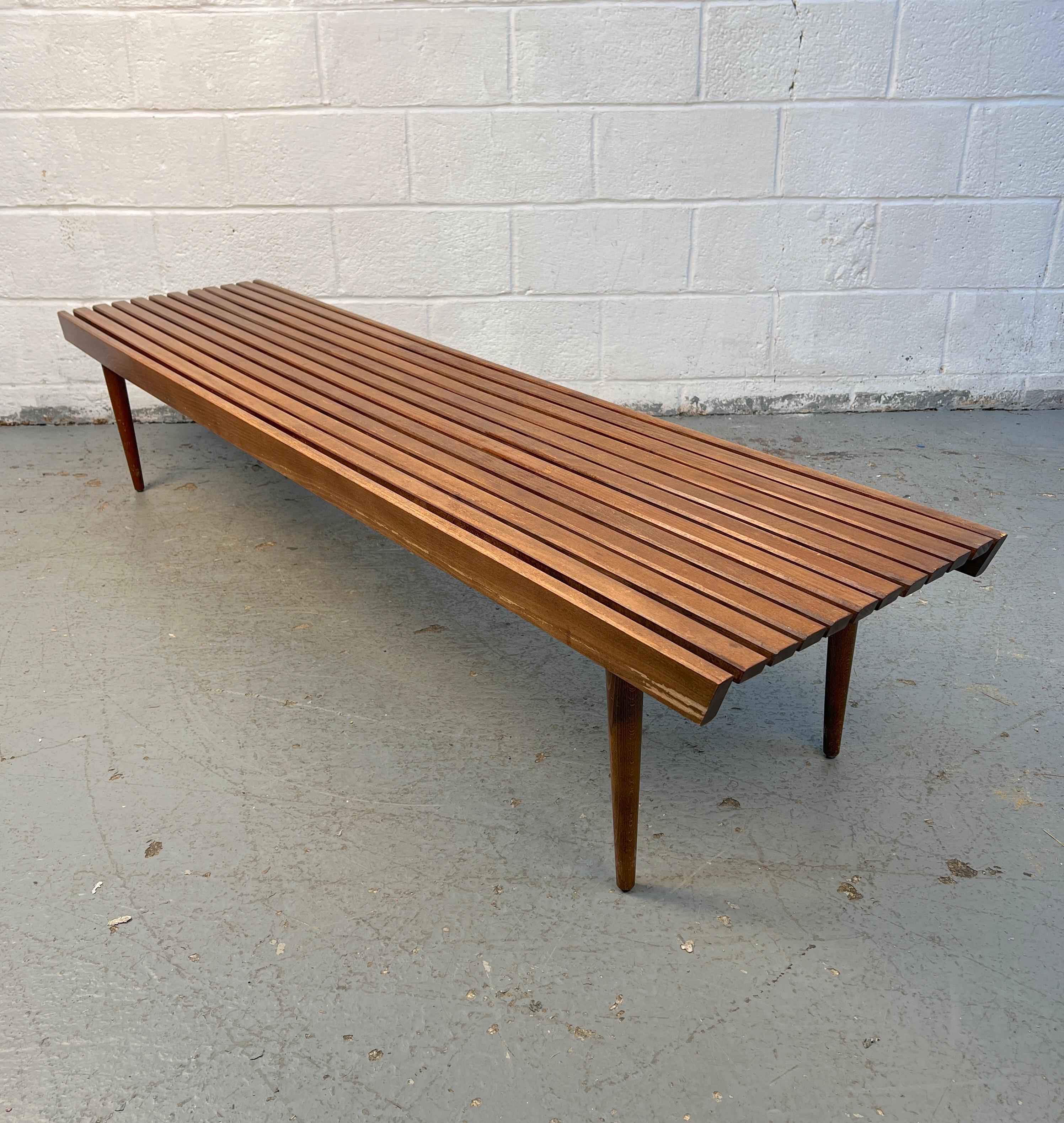 Klassische Lattenbank aus der Mitte des Jahrhunderts, gefertigt aus massivem Nussbaumholz, mit einer stromlinienförmigen Form und einer schönen natürlichen Maserung. Durch sein vielseitiges Design kann er als Sitzgelegenheit, Couchtisch oder als