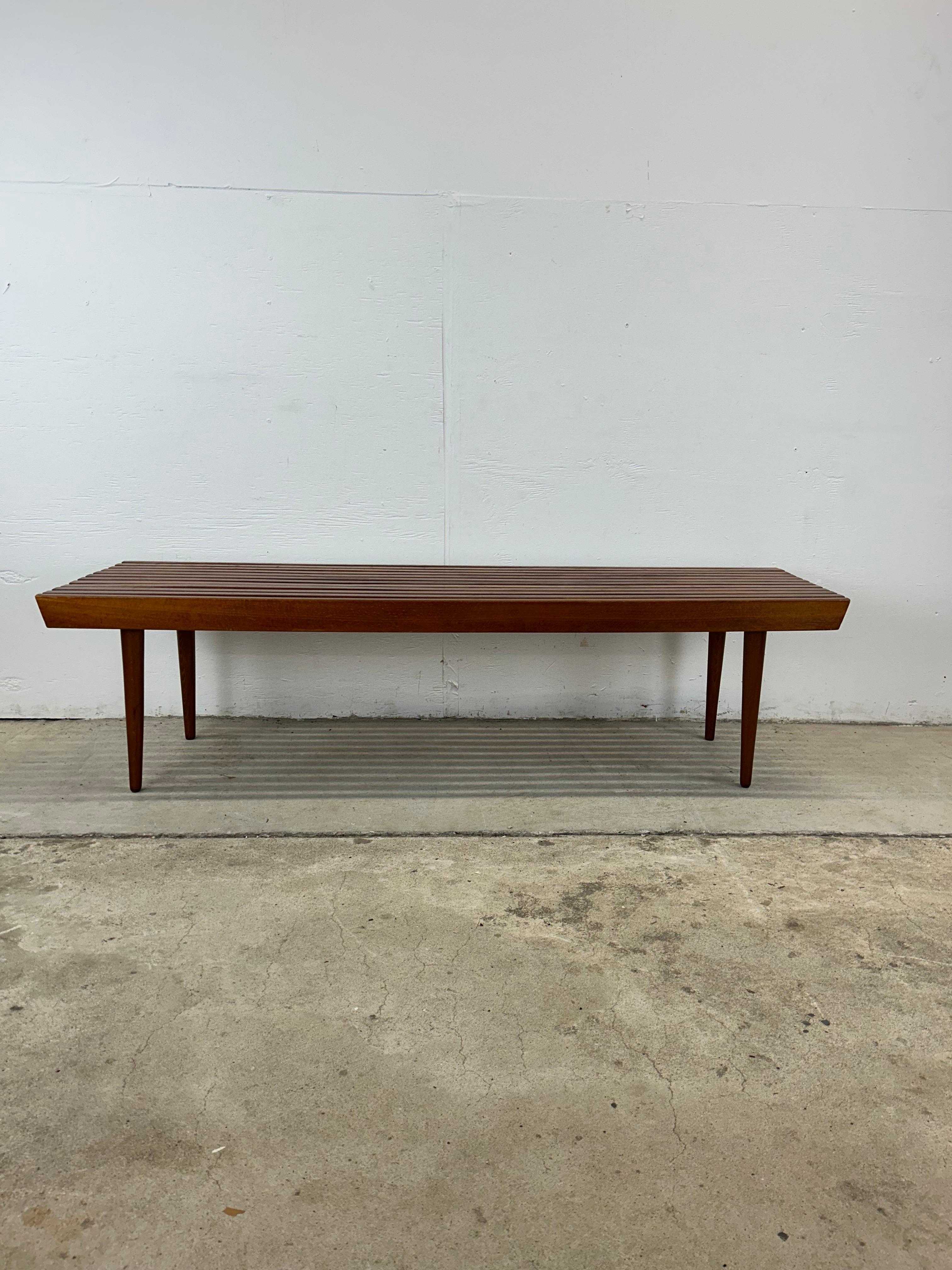 Cette table basse à lattes de style moderne du milieu du siècle est construite en bois dur, avec une finition originale en noyer et de grands pieds effilés.

Dimensions : 60w 18.25d 16h

Notes sur l'état : La finition d'origine est en bon état avec