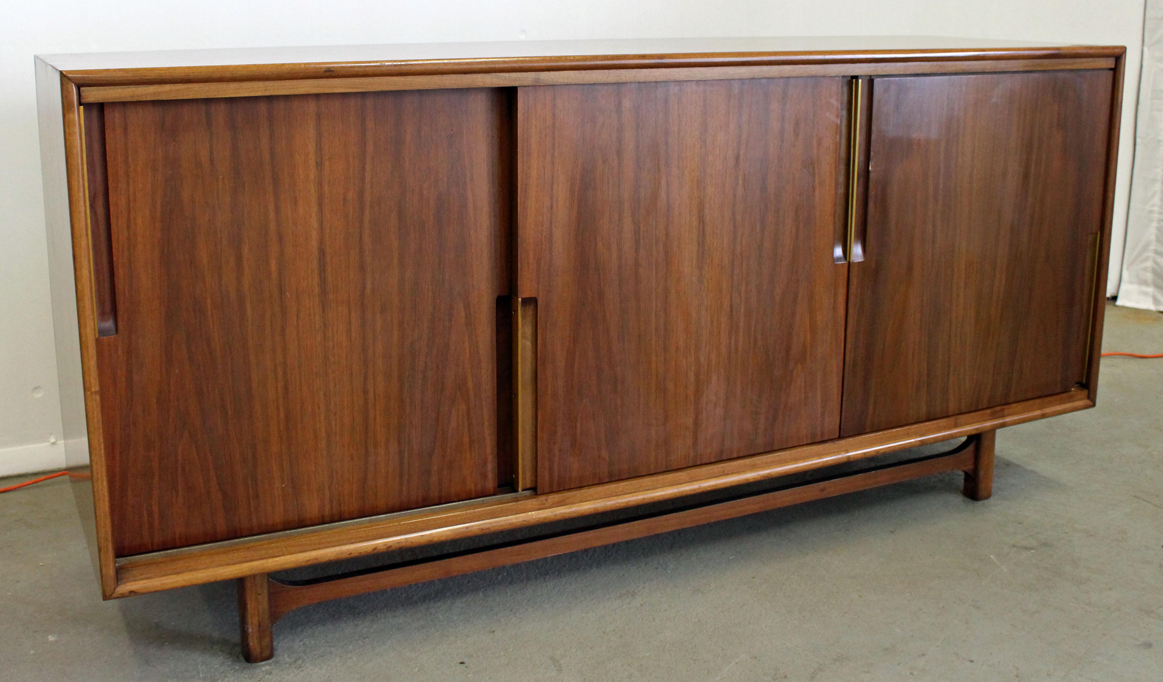 Offered is a Mid-Century Modern walnut credenza by Cavalier. Features nine drawers behind removable sliding doors with brass trim inset handles, a sculpted stretcher, and attractive walnut grain. Can be used as a dresser, sideboard or credenza. It