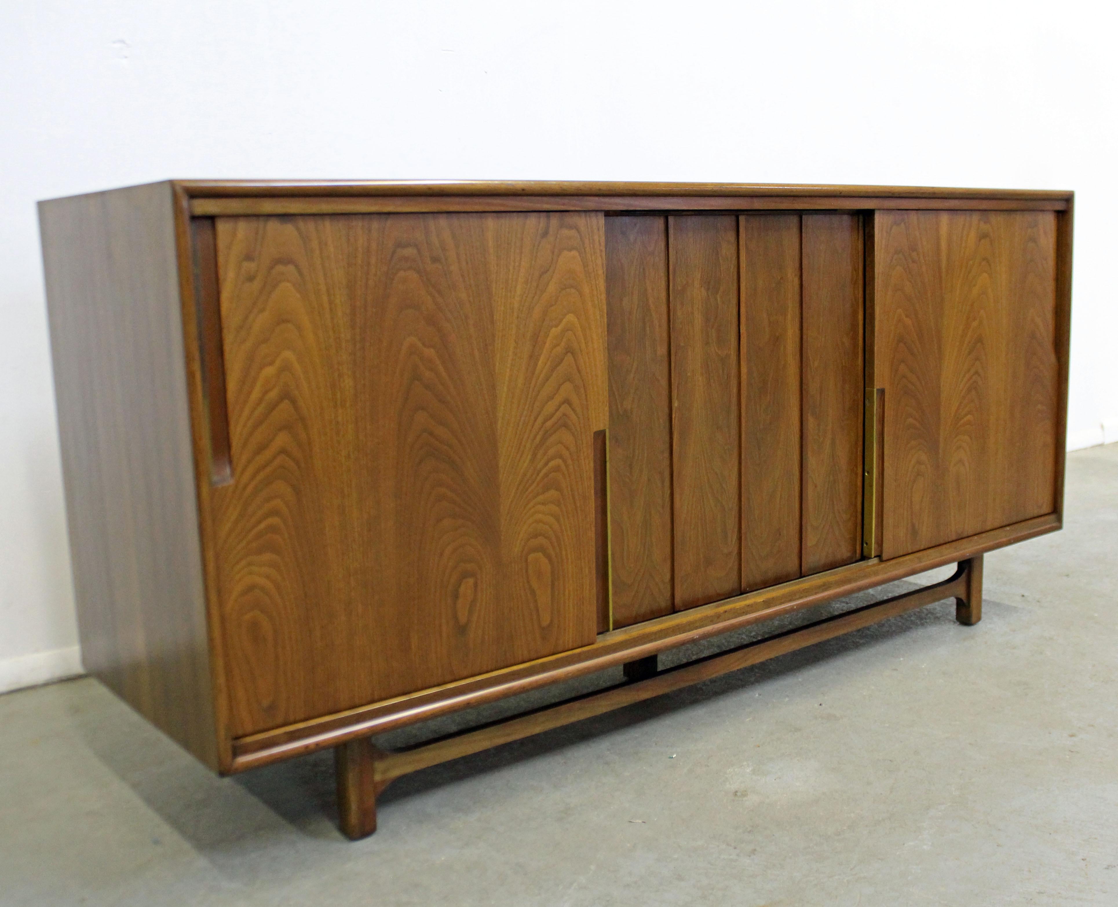 Offered is a vintage Mid-Century Modern walnut credenza by Cavalier. Features three sliding doors with storage inside: four drawers on the left, two drawers and a pull-out shelf in the middle and adjustable shelving on the right. The top left drawer