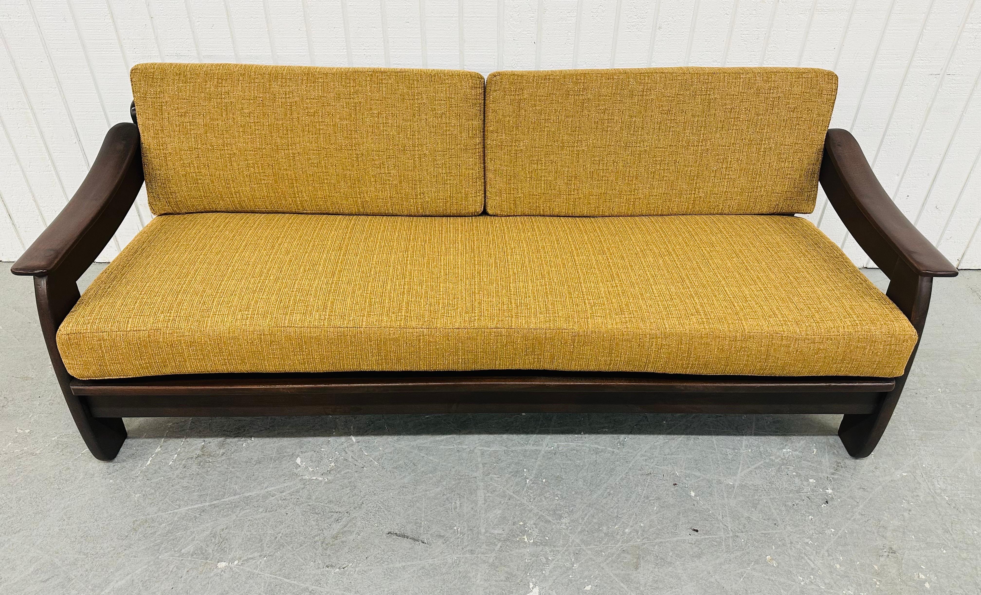 This listing is for a Mid-Century Modern Walnut Sofa. Featuring a wooden frame, curved arms, newly golden upholstered cushions, and a beautiful dark walnut finish. This is an exceptional combination of quality and design!