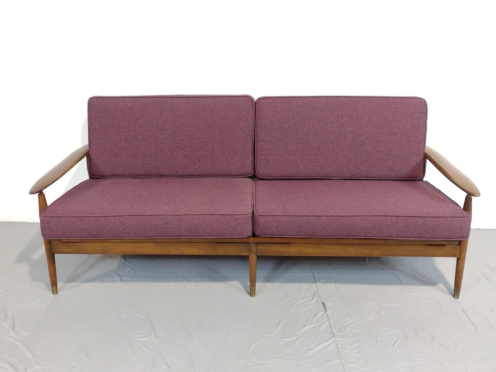 Questo divano vintage Mid-Century Modern presenta una struttura in noce massiccio con gambe affusolate e braccioli scolpiti. I cuscini sono rivestiti in un ricco tessuto color prugna.
