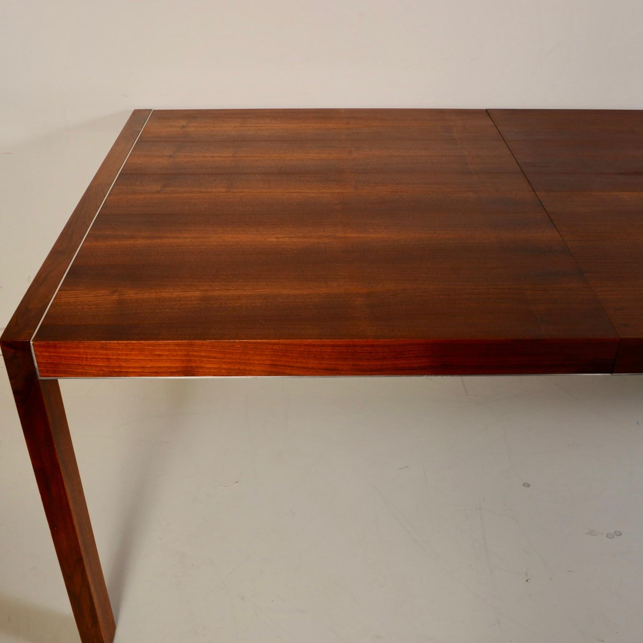 Large dining table that features a great bookmatched walnut veneer, trimmed in stainless steel; insets on each top end and along skirt. Made in Canada in the seventies, this has always had a felt cover over it whenever not in use. Table is just