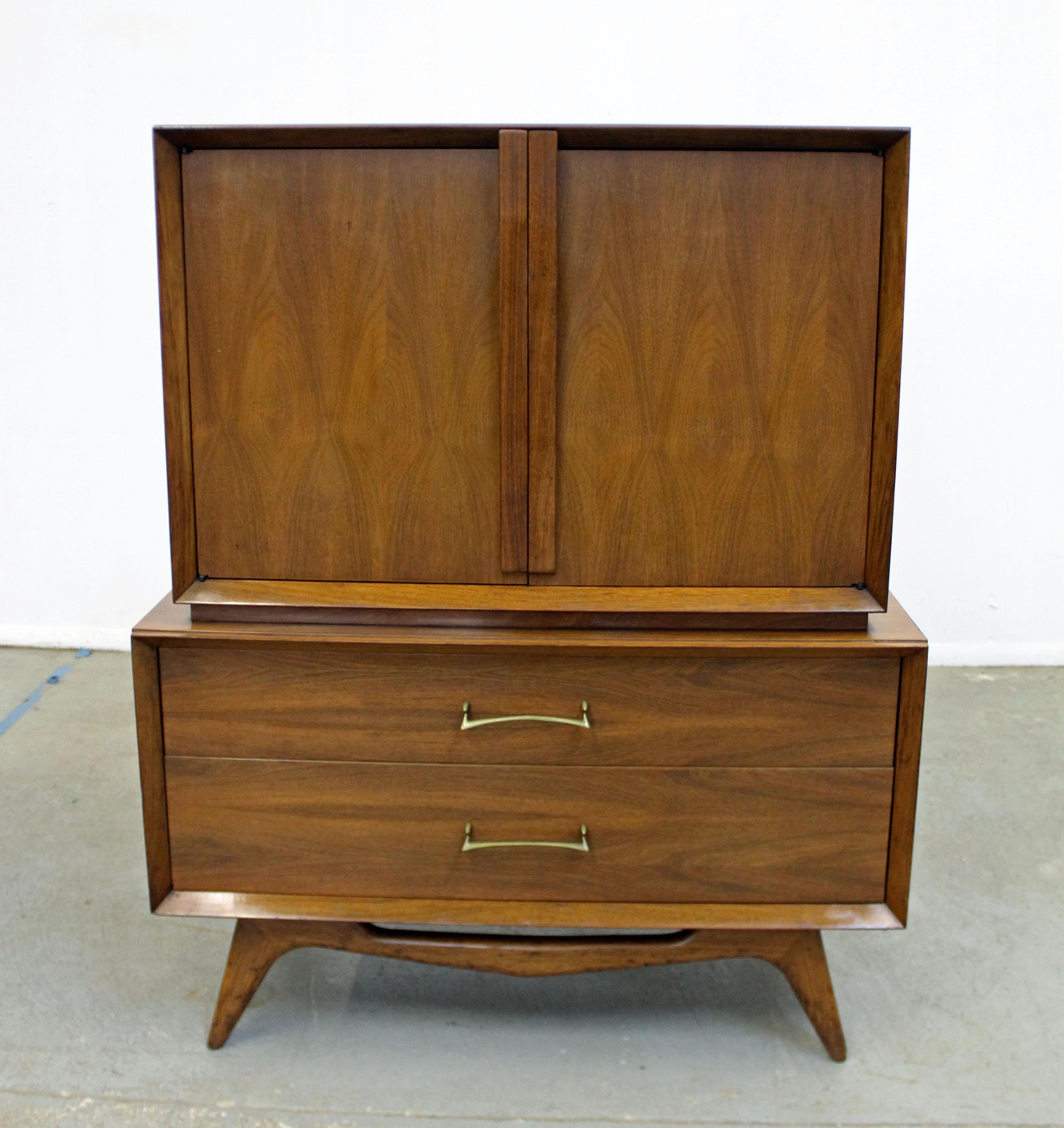 Offered is a beautiful Mid-Century Modern tall chest with ample storage space, fearturing two large bottom drawers and three top drawers behind doors with sculpted pulls. This piece is made of walnut. It is in good vintage condition with some