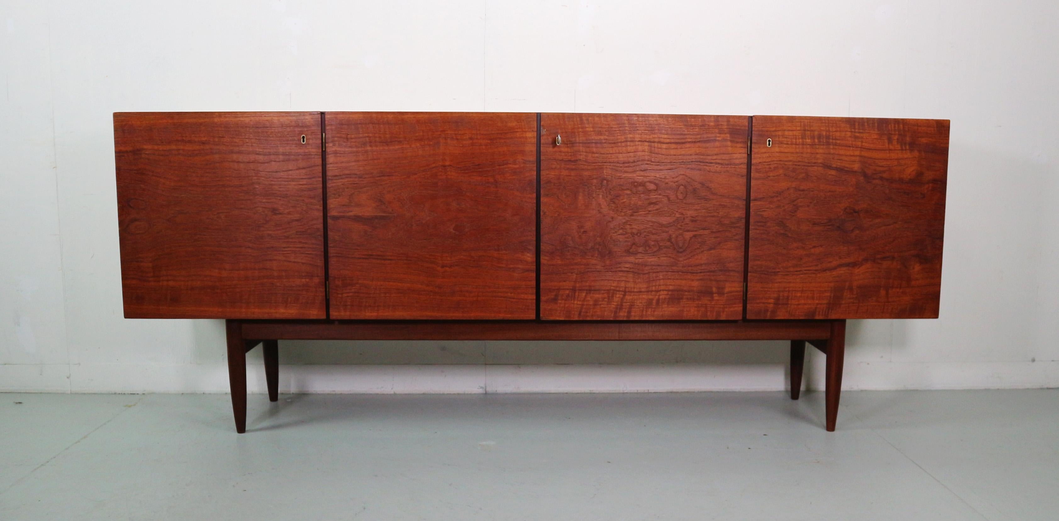Scandinavian Modern period sideboard produced in 1960's Denmark. 
Four doors and behind yhe right door four drawers in black and white.
The patterns of the wood is very beautiful.
Solid frame and feet.
All the locks are working with one key.

After