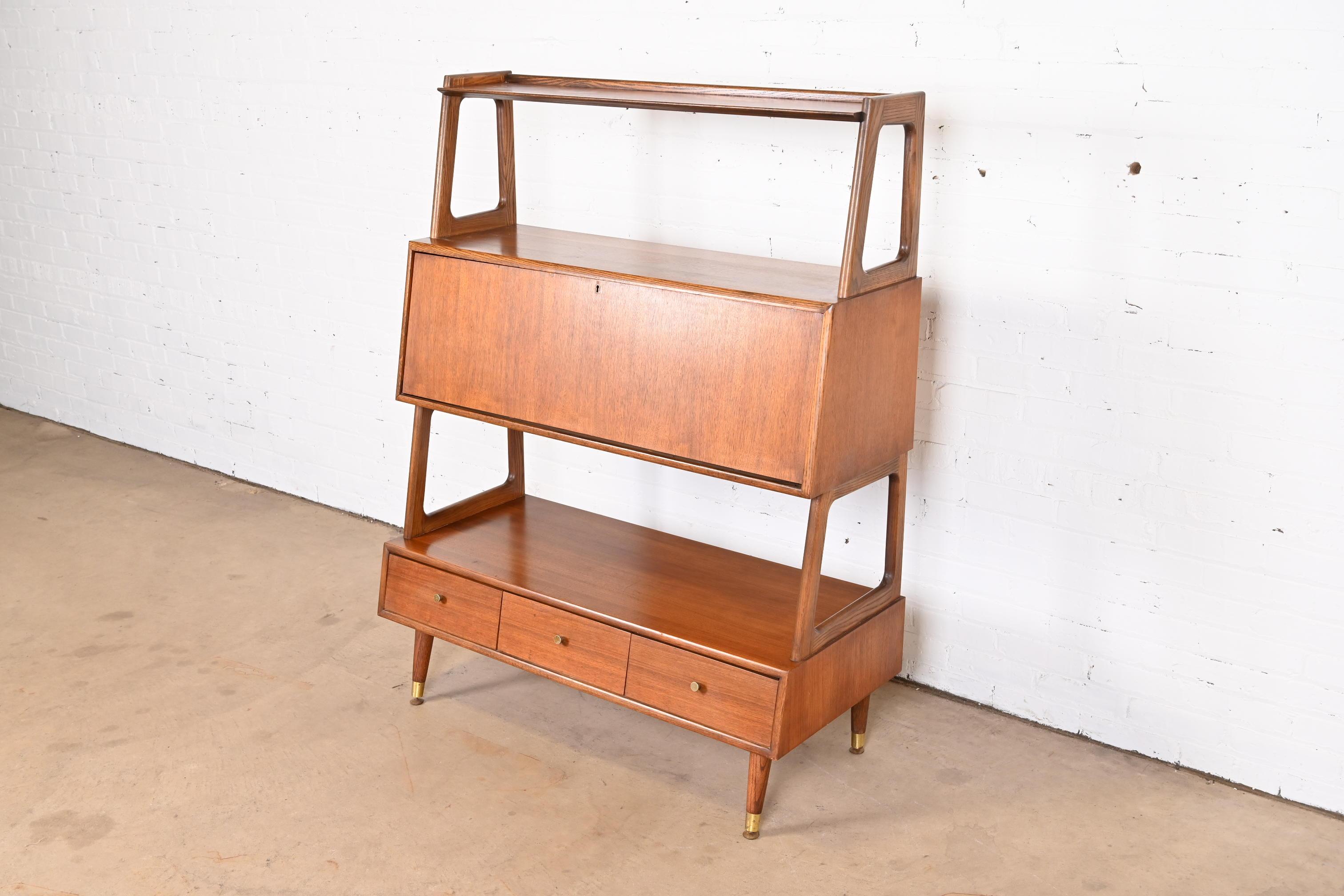 An exceptional Mid-Century Modern bookcase wall unit, room divider, or etagere with slant front secretary desk.

By Saginaw Furniture

USA, 1950s

Sculpted walnut, with brass hardware and capped feet.

Measures: 43