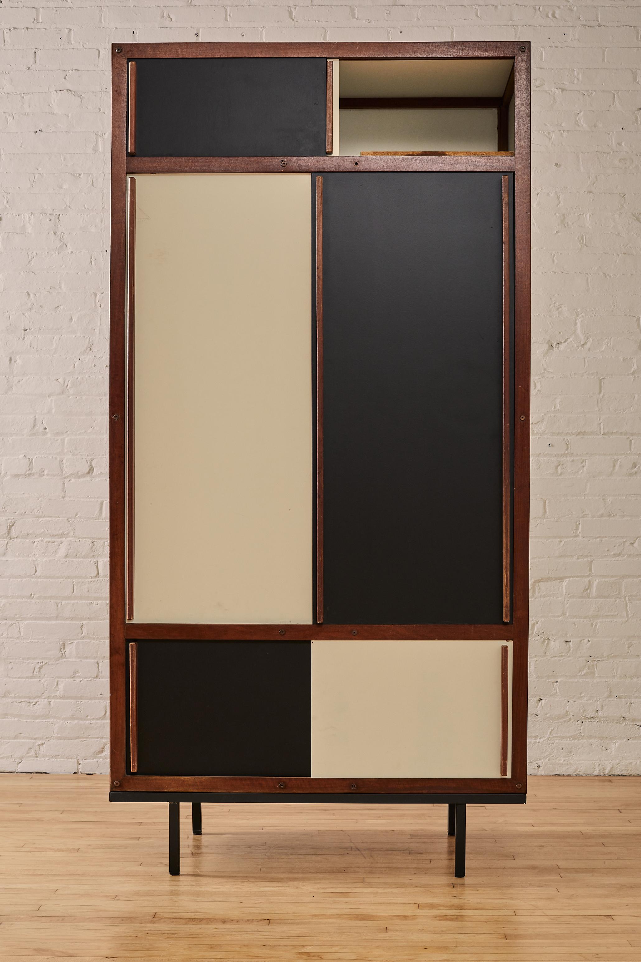 Mid Century Modern Wardrobe by André Sornay adorned with black and white sliding doors. The wardrobe rests atop a sleek black metal base. Inside, the André Sornay is a hanging bar to help arrange your clothing with care, while well-placed shelving