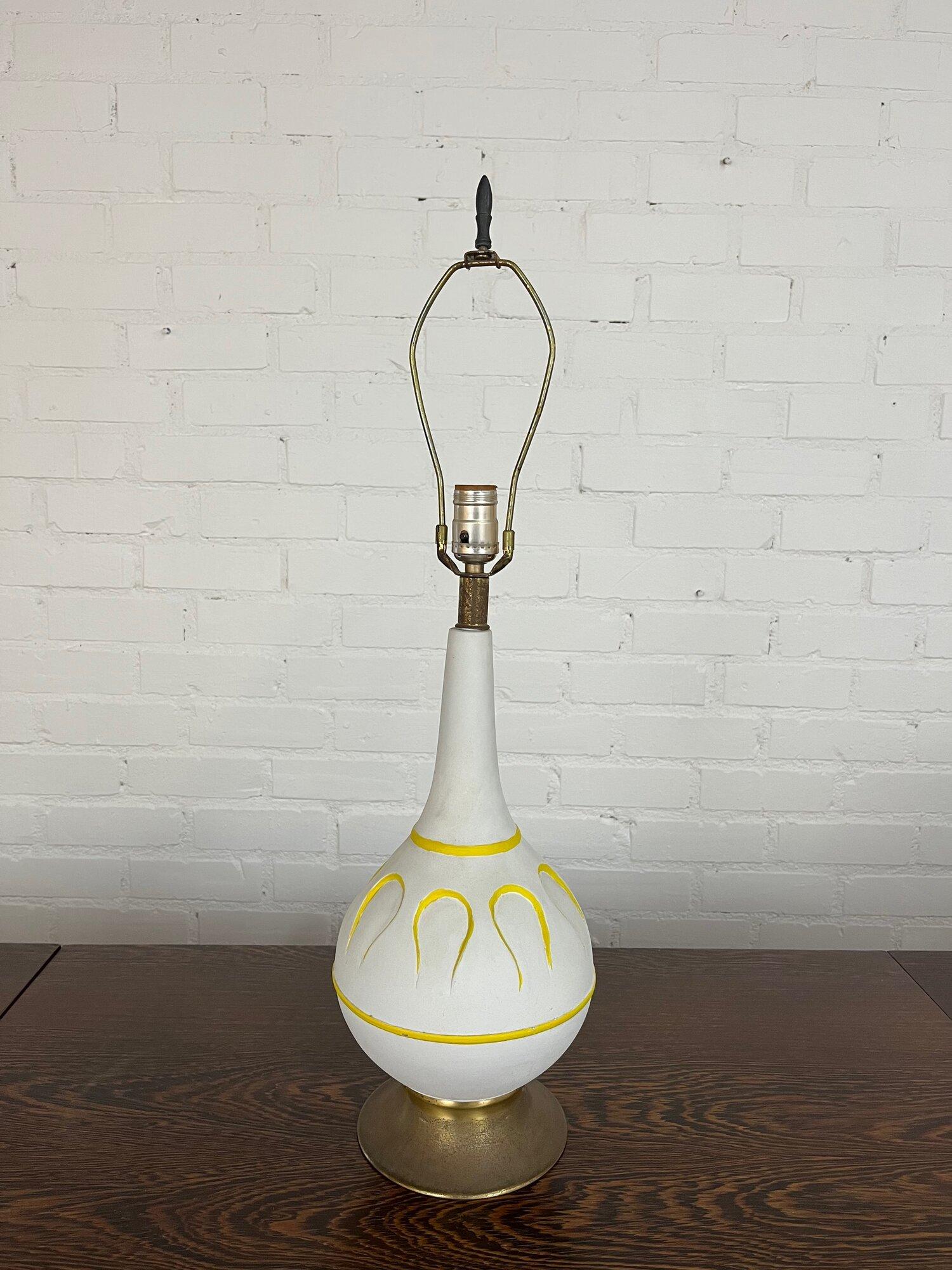 Measures: W7.5 D7.5 H29

Vintage table lamp with matte white finish accented by yellow details following the pattern on the table lamp. The brass base and details have patina. The lamp turns on and off at neck. Lamp is fully functional.