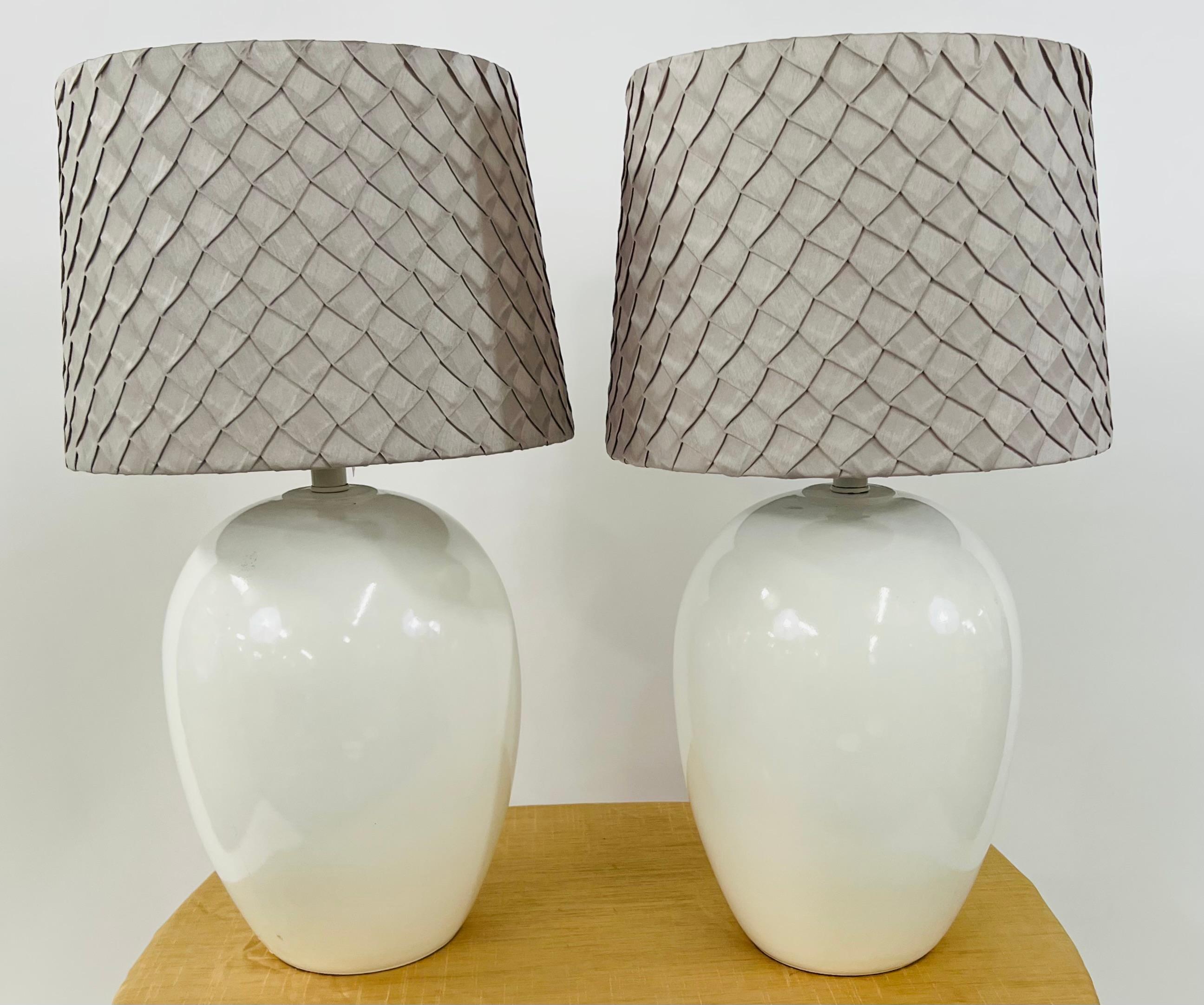 A pair of Mid-Century Modern ceramic table lamps. The beautiful lamps feature a minimalistic design in white color. The shades are custom and new. The lamps will complement the style of any room or style. Elegant , the neutral colors of the lamp and