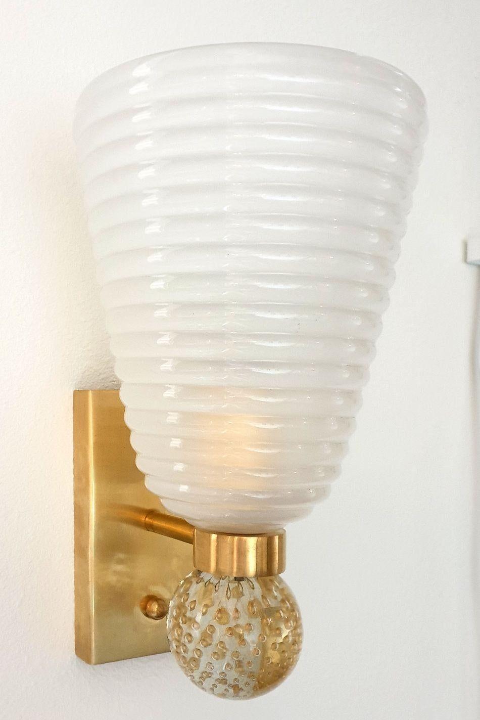 Pair of neoclassical style Murano glass wall sconces, attributed to Cenedese, Italy, circa 1980s.
The Mid-Century Modern sconces are made of a frosted Murano glass shade, nesting the light bulb.
The mounts are in solid brass; and they have a clear