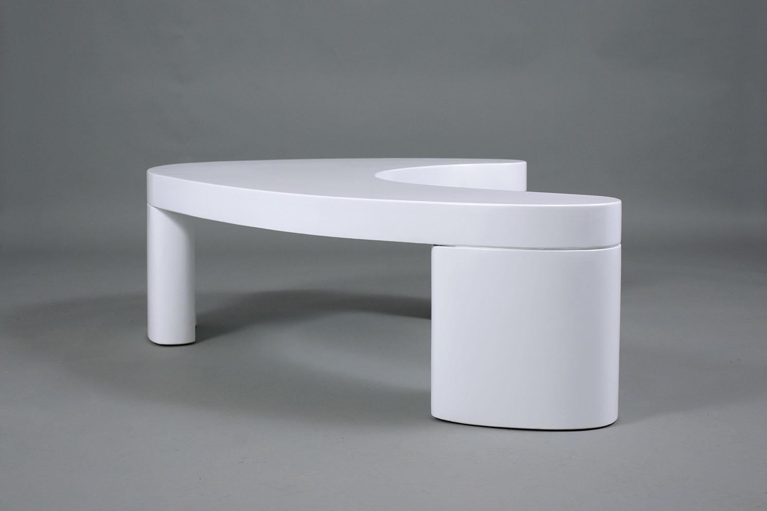 A remarkable Mid-Century Modern coffee table features a kidney-shaped design and has been professionally restored and newly stained in a white lacquer finish. This unique table sits on three oval pedestal legs and is the perfect addition to a