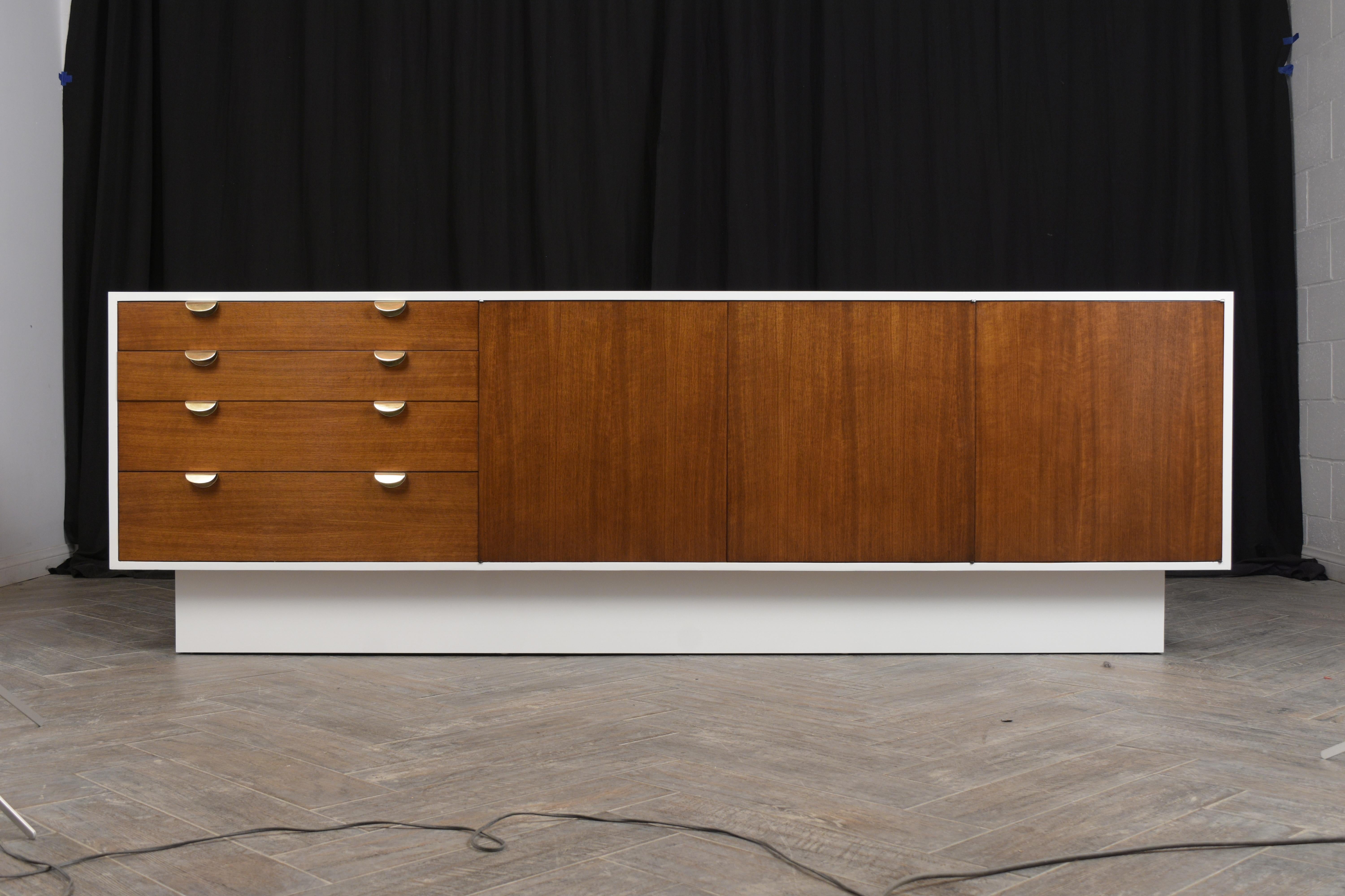 This large Mid-Century Modern credenza has been professionally restored, stained in walnut and white combination, and has a newly lacquered finish. The credenza features four top drawers with dual sold brass handles, two center doors with two