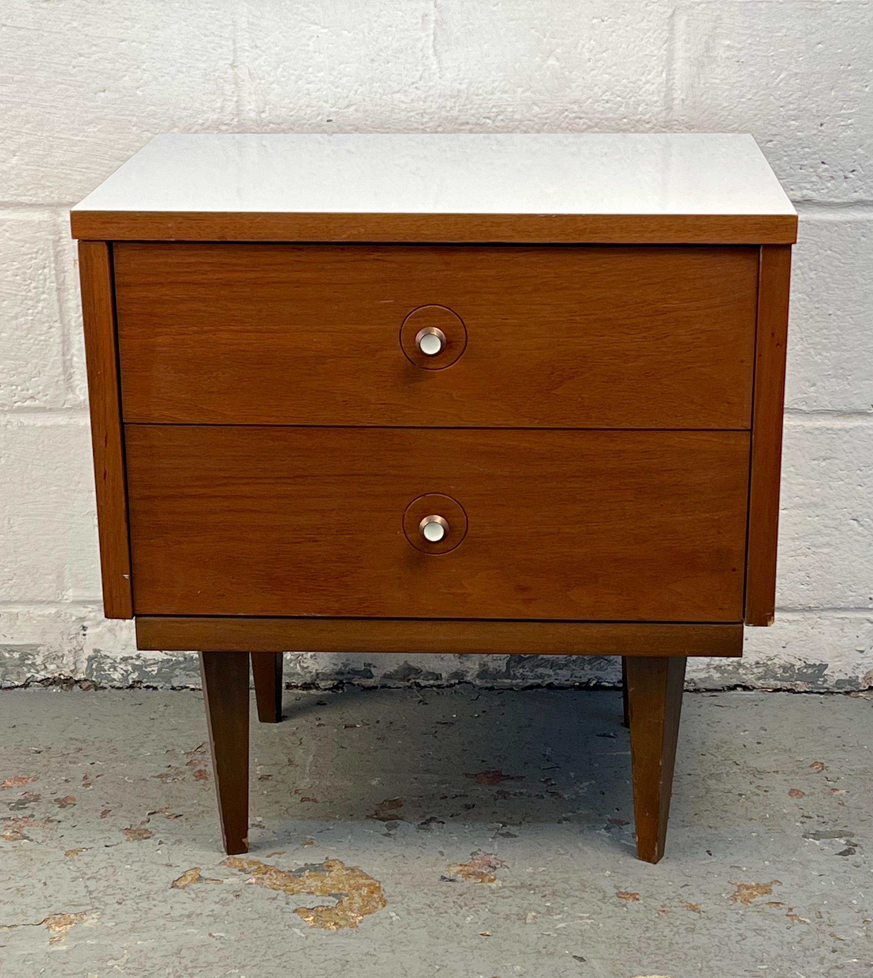 Table de nuit élégante fabriquée en noyer riche, avec un profil élégant accentué par un dessus blanc contrasté. Sa forme épurée et ses rangements pratiques en font un complément polyvalent et attrayant pour la chambre à coucher ou l'espace de