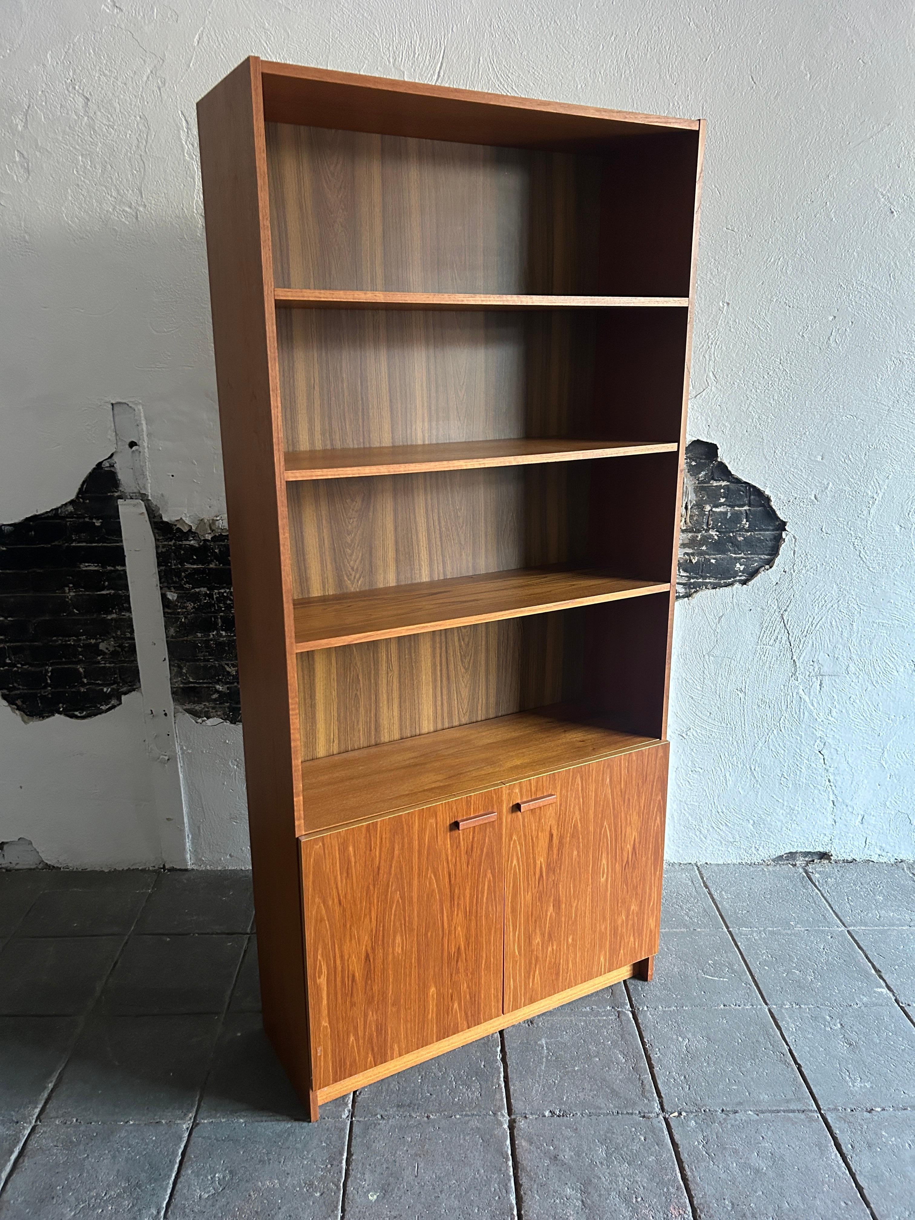 Stunning Mid-Century Modern wide teak tall bookcase with (2) cabinet doors Made in Denmark. This bookcase is completely original and in very good vintage condition. The bookcase has (2) adjustable shelves with (5) shelves total and lower cabinet