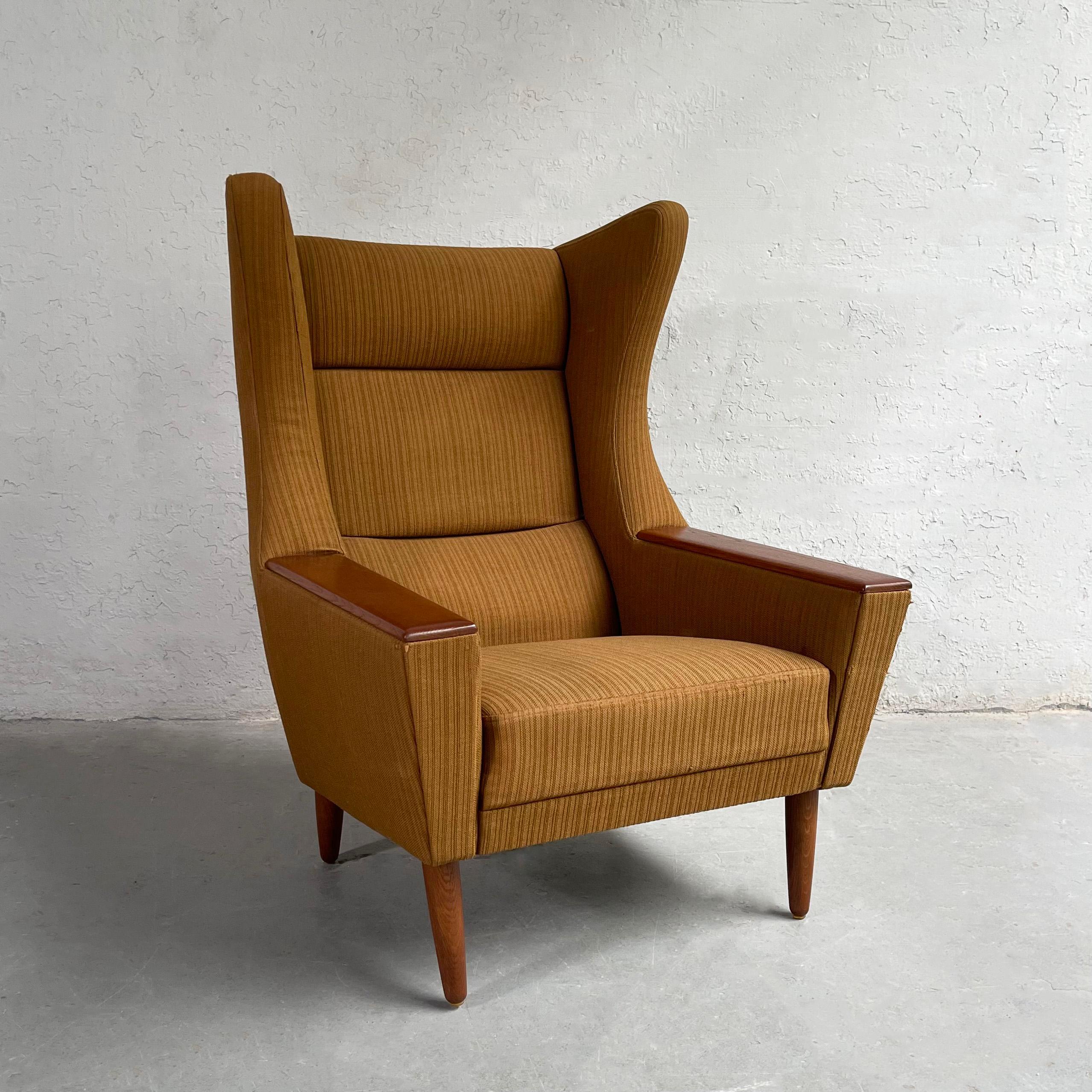 Cozy and enveloping, Mid-Century Modern, wingback lounge chair boasts a striking Silhouette from all angles. The chair features it's original ribbed wool upholstery with oak armrests and tapered legs.