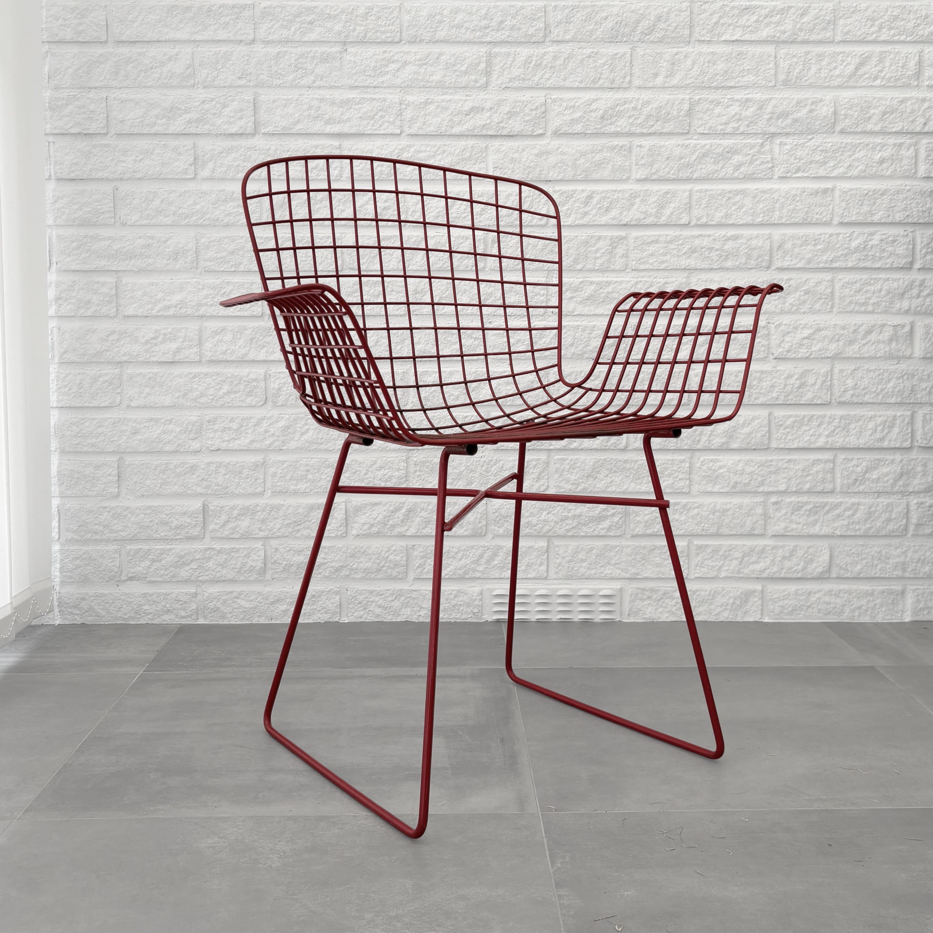 A modernist wire armchair crafted from robust steel wire painted in a deep red color. The chair is constructed from a sled shaped base holding a sculptural wire seat. The base can be detached and reattached without the use of any tools, making the