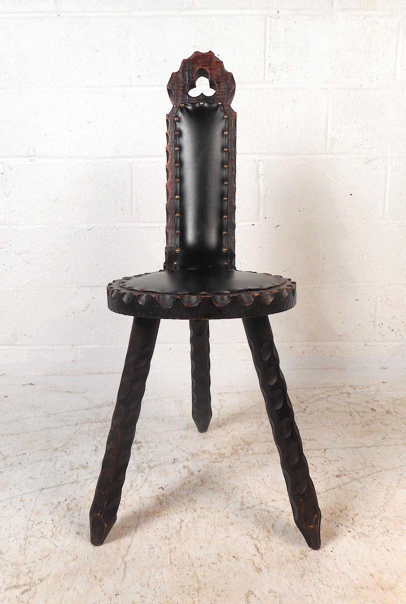 This stylish chair in the style of Witco features tripod legs and a carved wooden construction with beautiful natural grain which offers a rustic style to any room. The vinyl seat upholstery is secured with metal studs. Please confirm item location