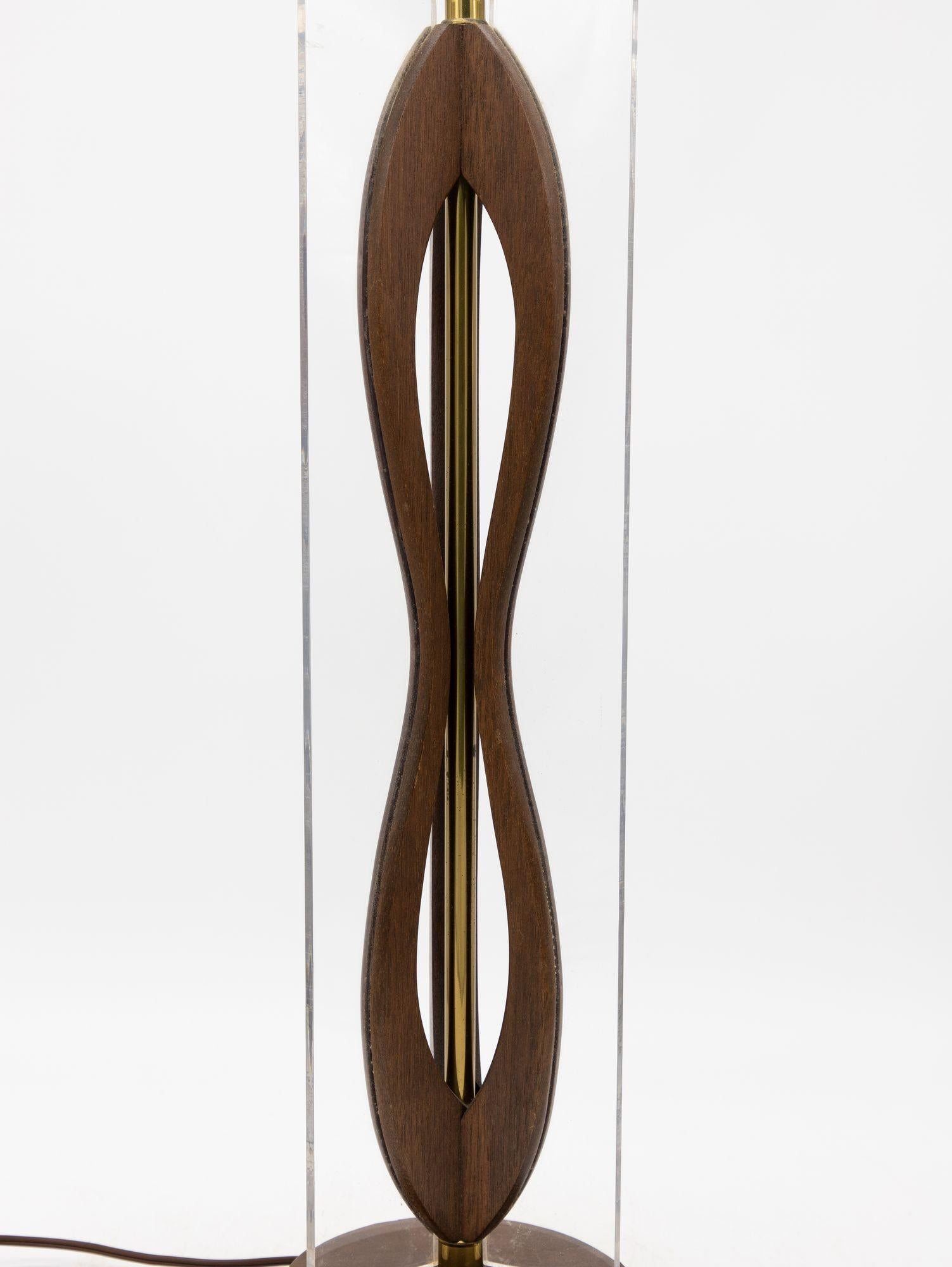 Cette étonnante lampe de table moderne du milieu du siècle présente un design innovant combinant le bois et la lucite. La base est composée de trois panneaux de bois sculpté ondulant, élégamment attachés à des panneaux rectangulaires en lucite,
