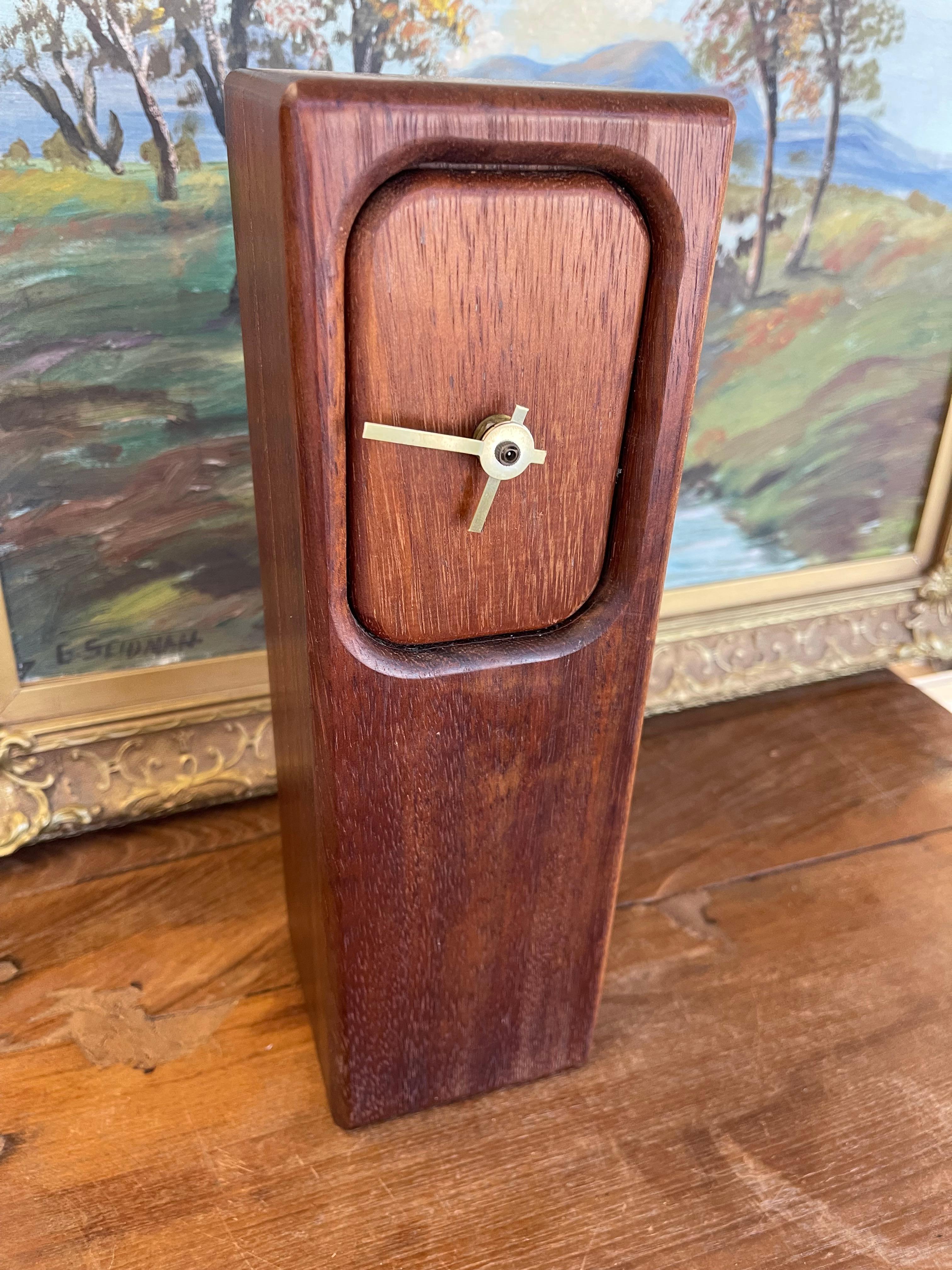 A sculptural mid-century modern wood block clock featuring a minimalist rectangular form with softly rounded corners at the clock face.The case is crafted from richly grained hardwood with a warm, natural finish that highlights the wood's texture