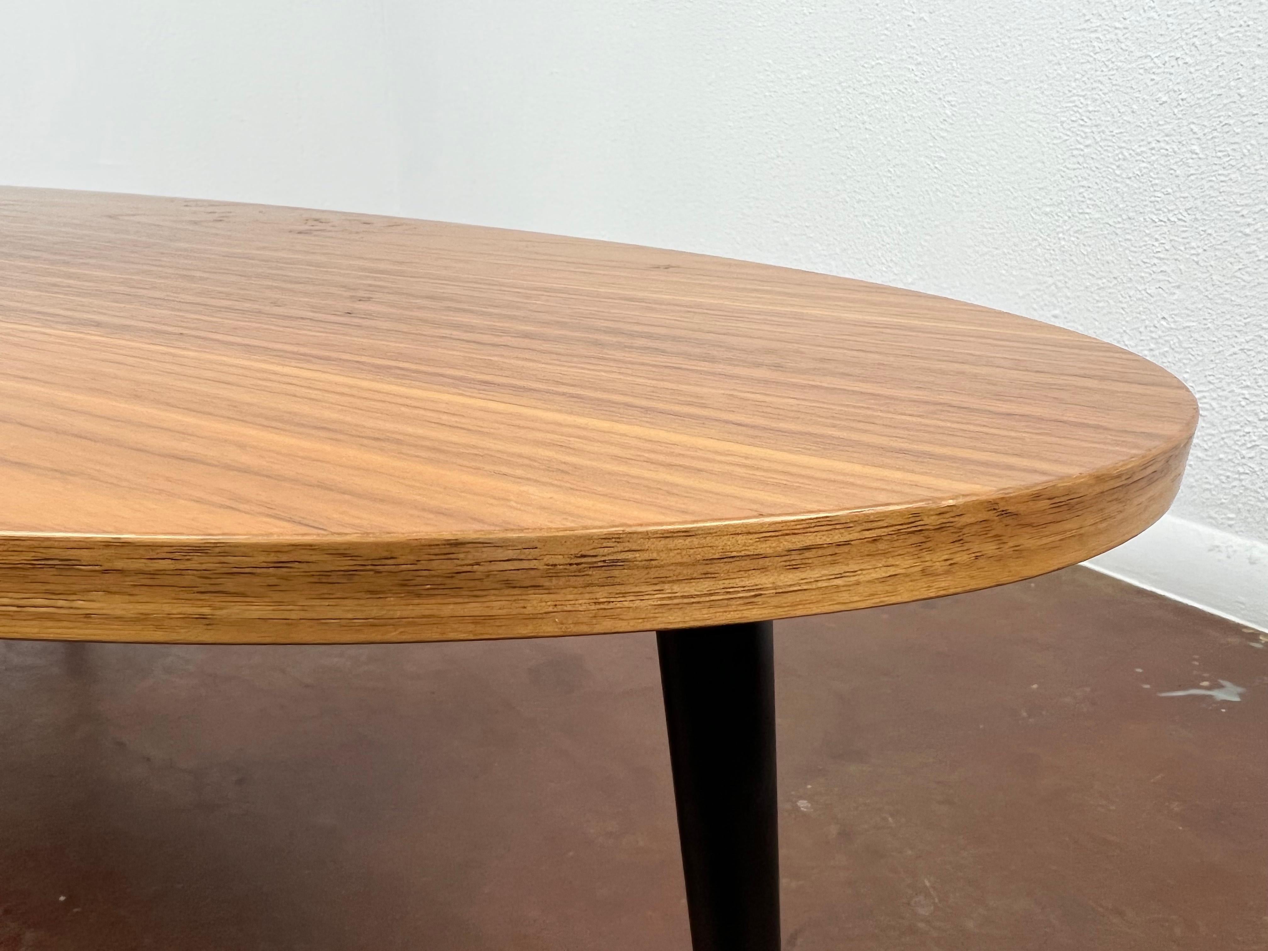 Sleek mid-century design solid wood surfboard coffee table. Features curved lip edge and 4 tapered turned legs. Sturdy and structurally sound. Has some expected slight finish wear and scratching.