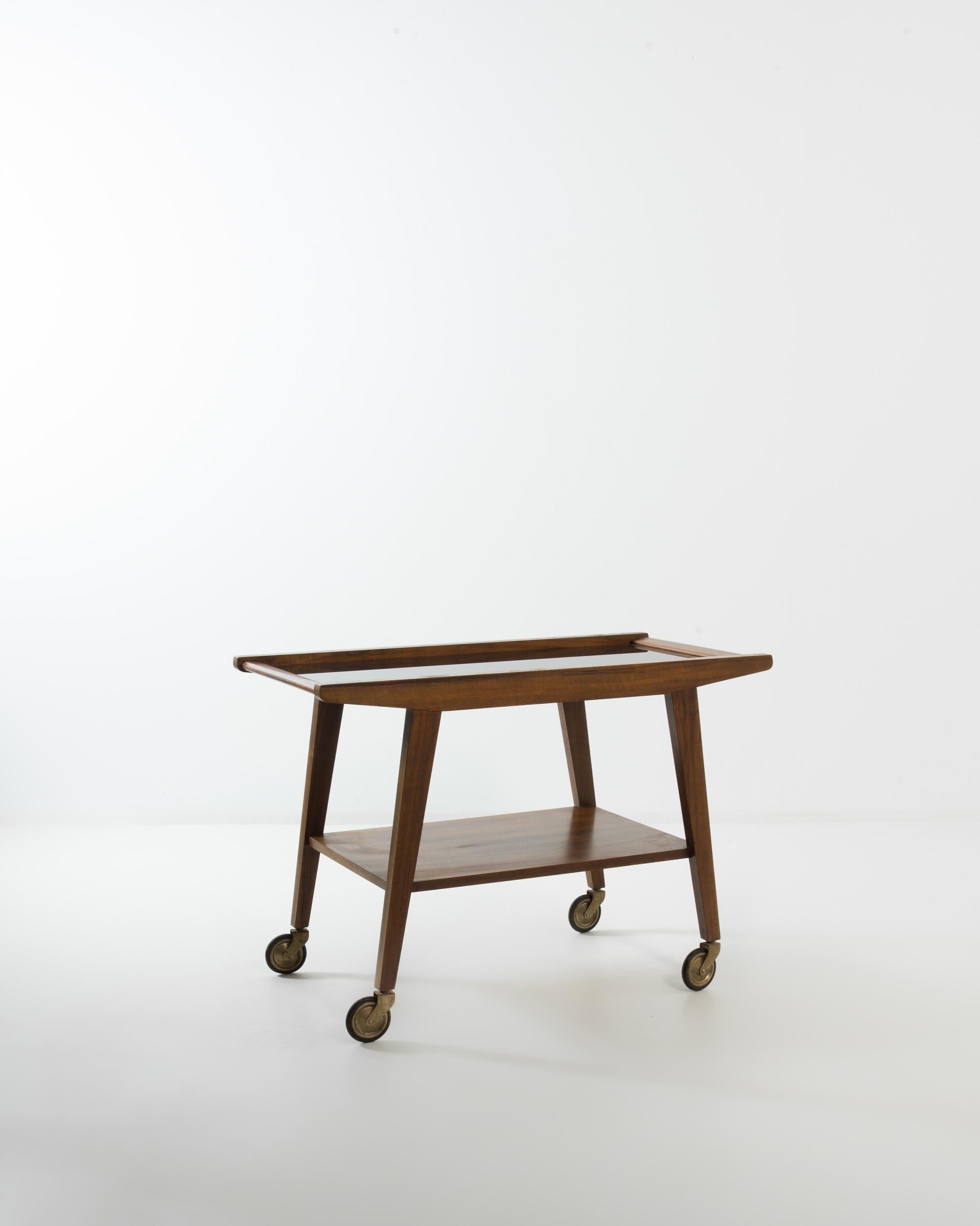 This beautiful Modernist bar cart is sure to become a treasured fixture in your home. Made in 20th century France, a streamlined design in warm, auburn-colored wood evokes a sense of leisure and ease. Tapered legs atop metal wheels form a trapezoid