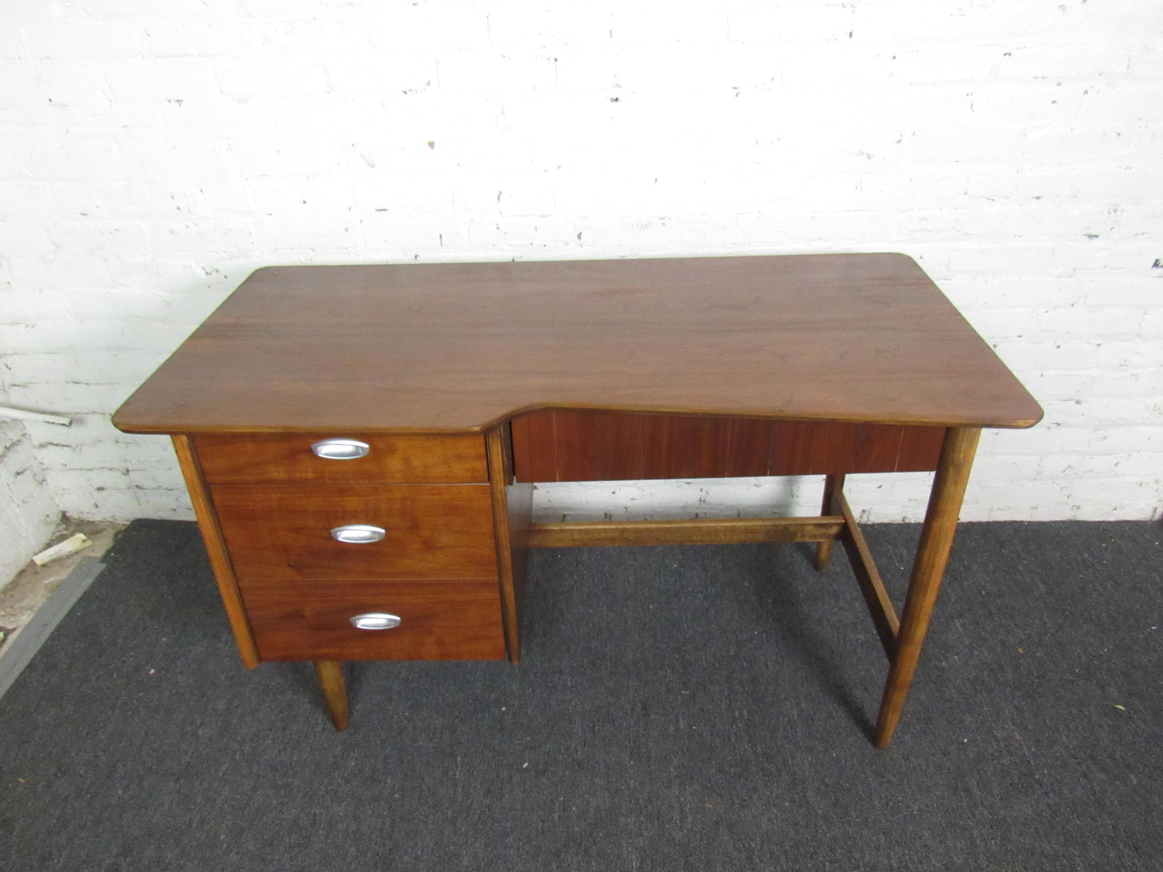 With three large drawers, sculpted legs, and a uniquely-shaped writing surface, this vintage desk is perfect for any home office or study. Beautifully refinished walnut woodgrain complements Mid-Century design to make this piece stand out anywhere.