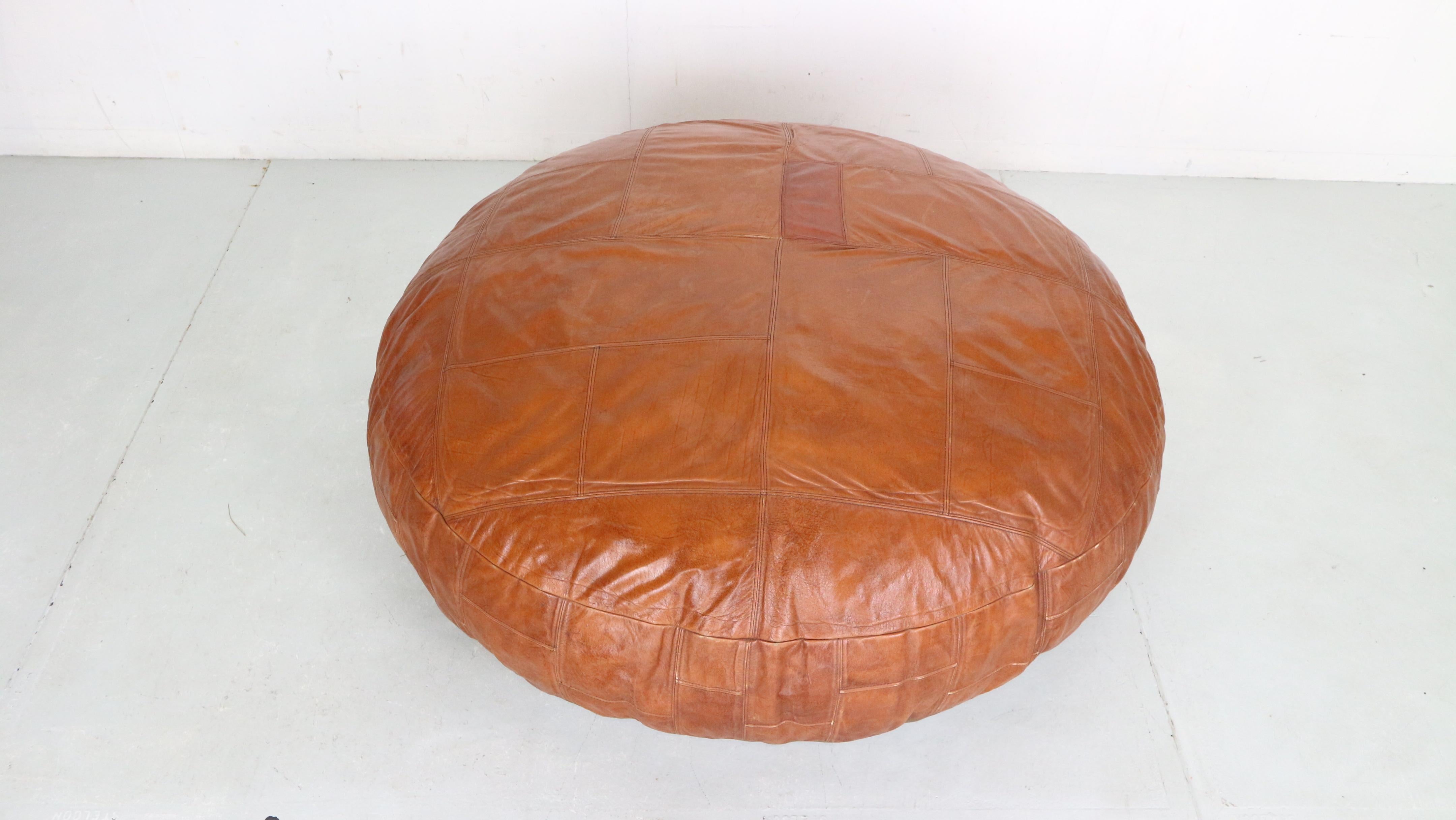 Mid century modern period cognac brown leather xxl pouf/ ottoman made in 1960's period.

XXXL (51 inch, 130cm) 

It’s style is a lot like the designs by Swiss company De Sede who is famous for their impressive leather work. 
The patchwork