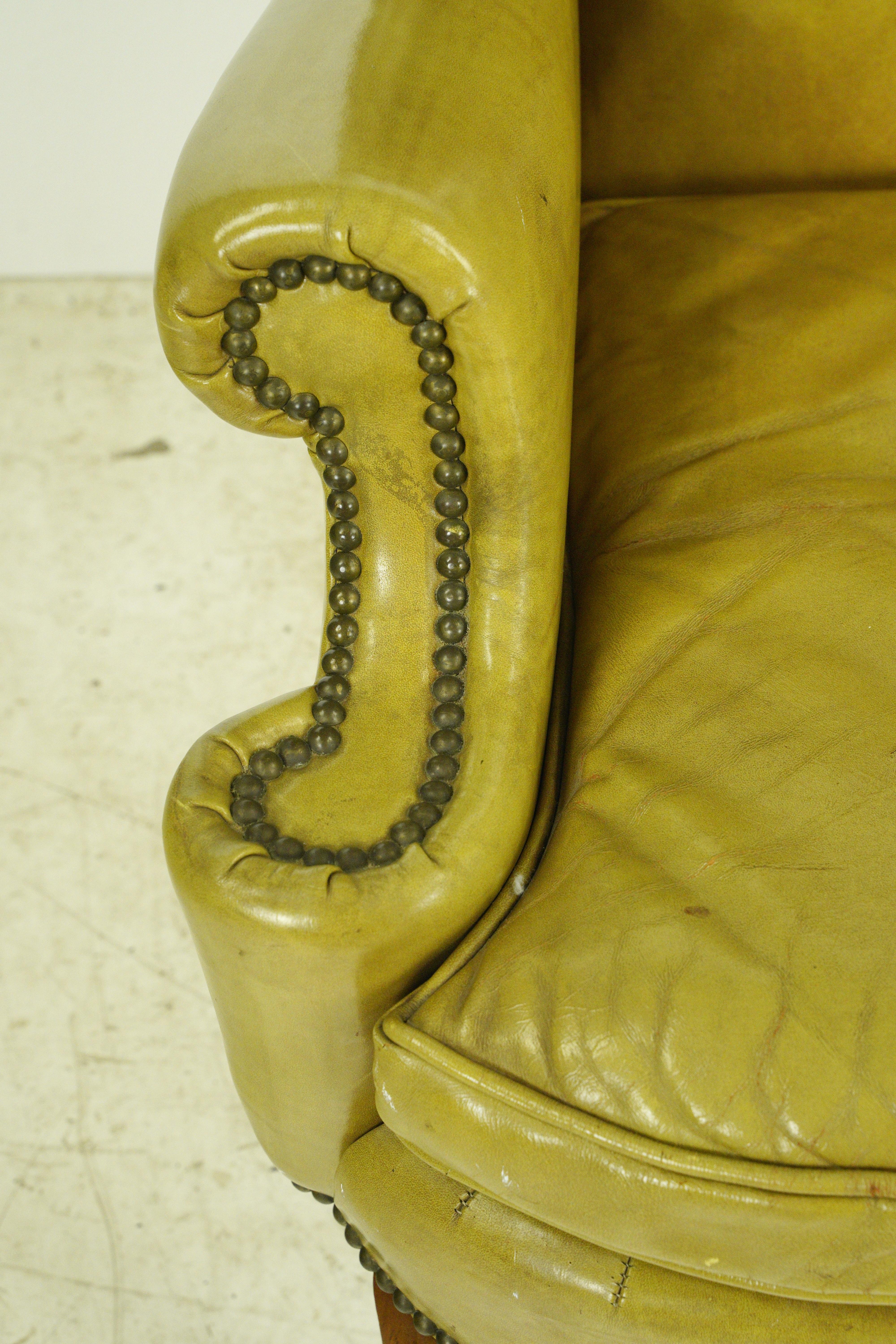 Mid-Century Modern wingback armchair made of yellow leather with studded details and wood legs. Good condition with surface wear from age. One available. Please note, this item is located in our Scranton, PA location.