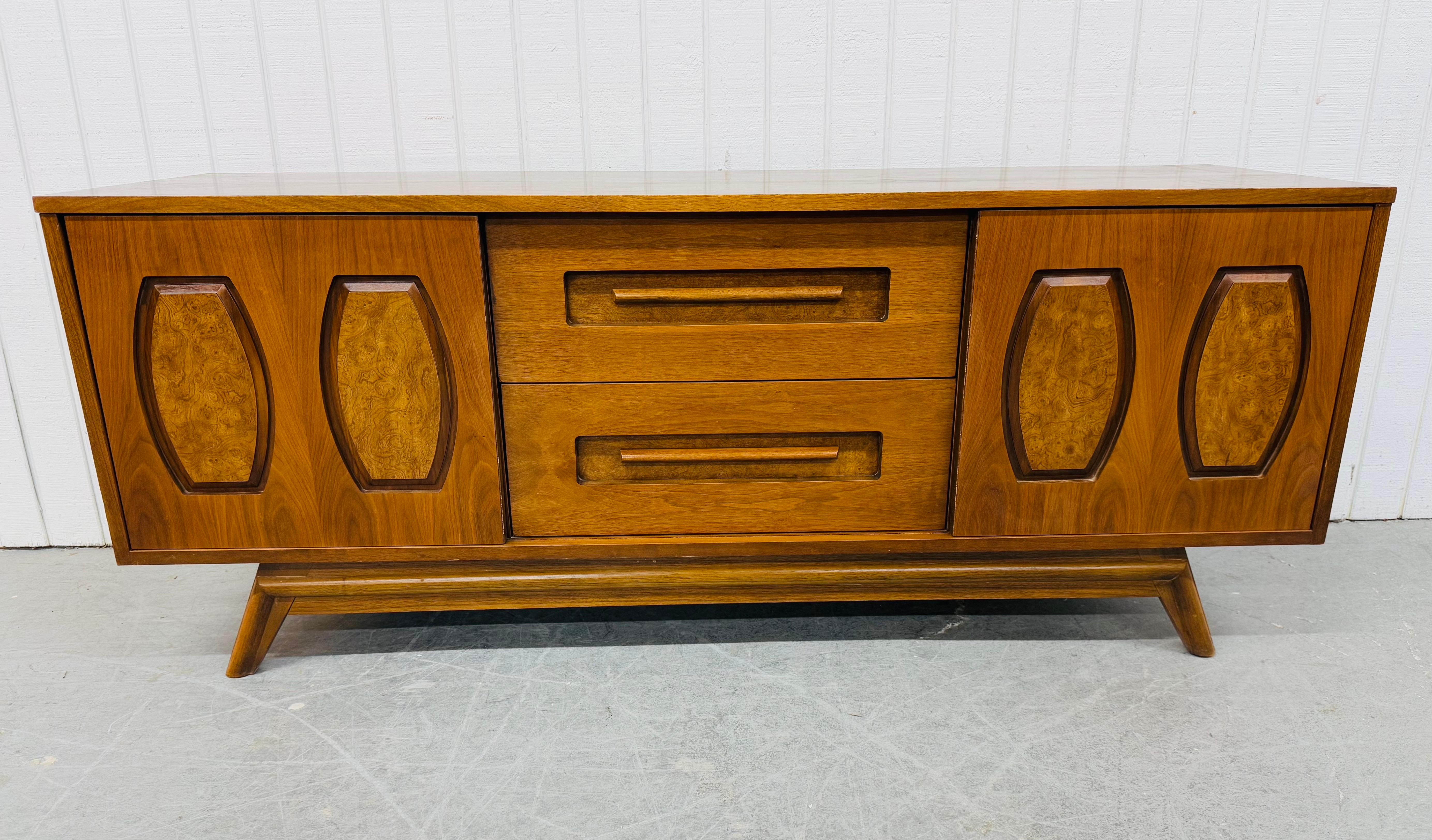 Questo annuncio si riferisce a una credenza in legno di noce della Young Manufacturing, un'azienda moderna di metà secolo. Caratterizzato da un design lineare, ante scorrevoli che si aprono su cassetti e spazi nascosti, due cassetti più grandi al