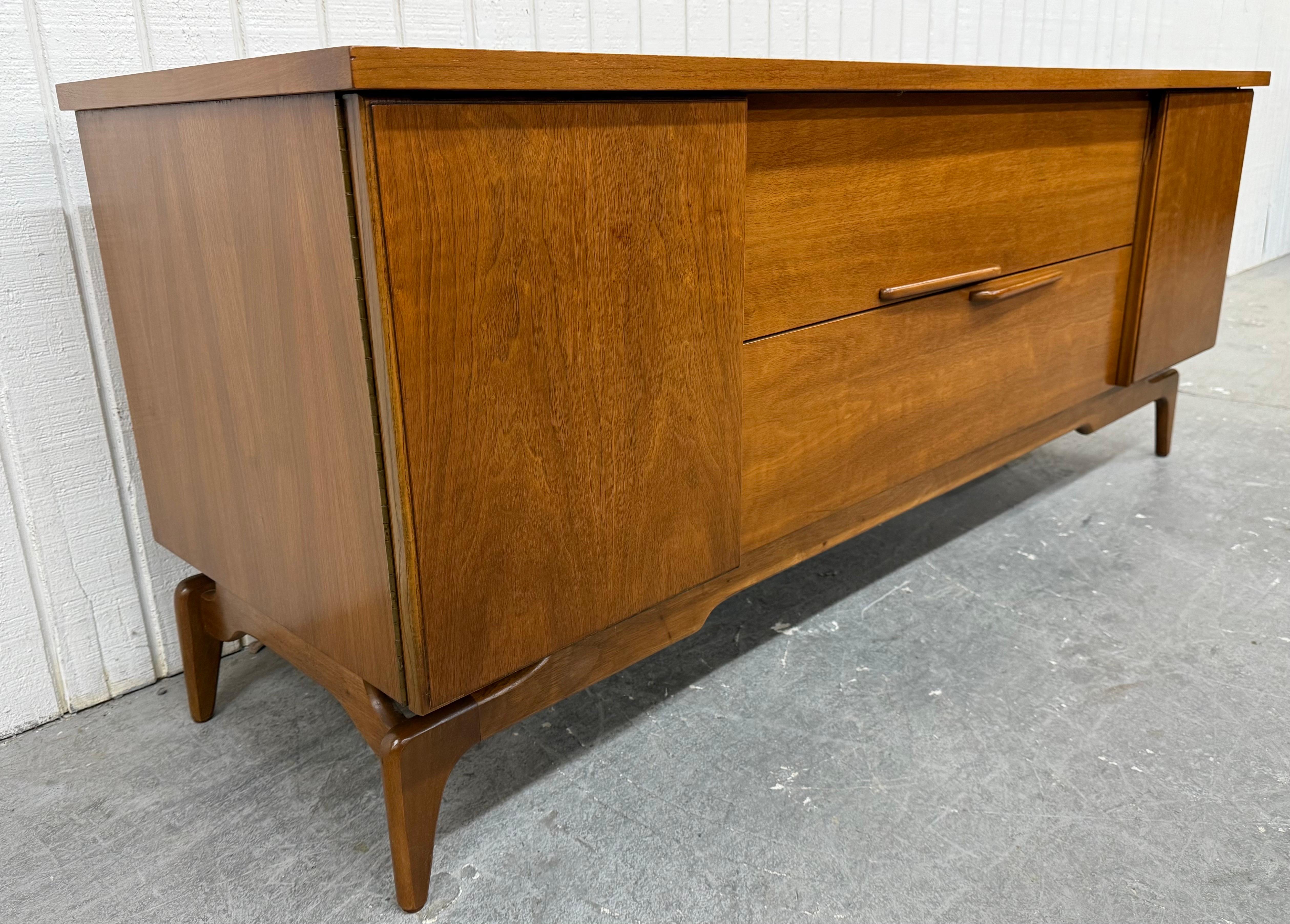 Questo annuncio si riferisce a una credenza in legno di noce della Young Manufacturing, un'azienda moderna di metà secolo. Design lineare, ante su ogni lato per riporre gli oggetti, due cassetti centrali con tiretti in legno, gambe moderne e una