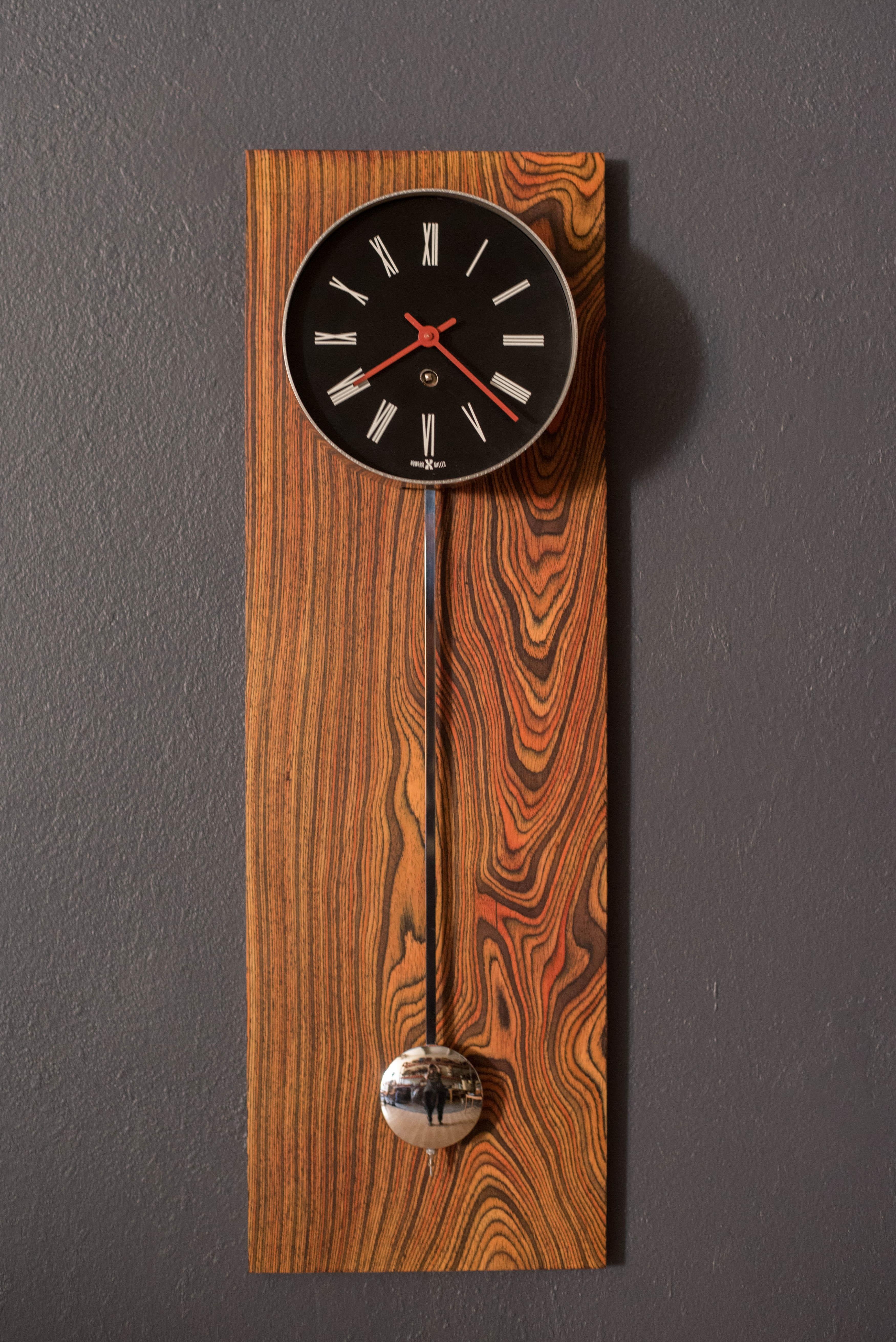 Vintage Pendulum Wall Clock manufactured by Howard Miller, circa 1970's. This stand out piece features stunning zebra wood grains and a polished chrome pendulum. Keeps time with an 8 day movement and includes the wind up key. 