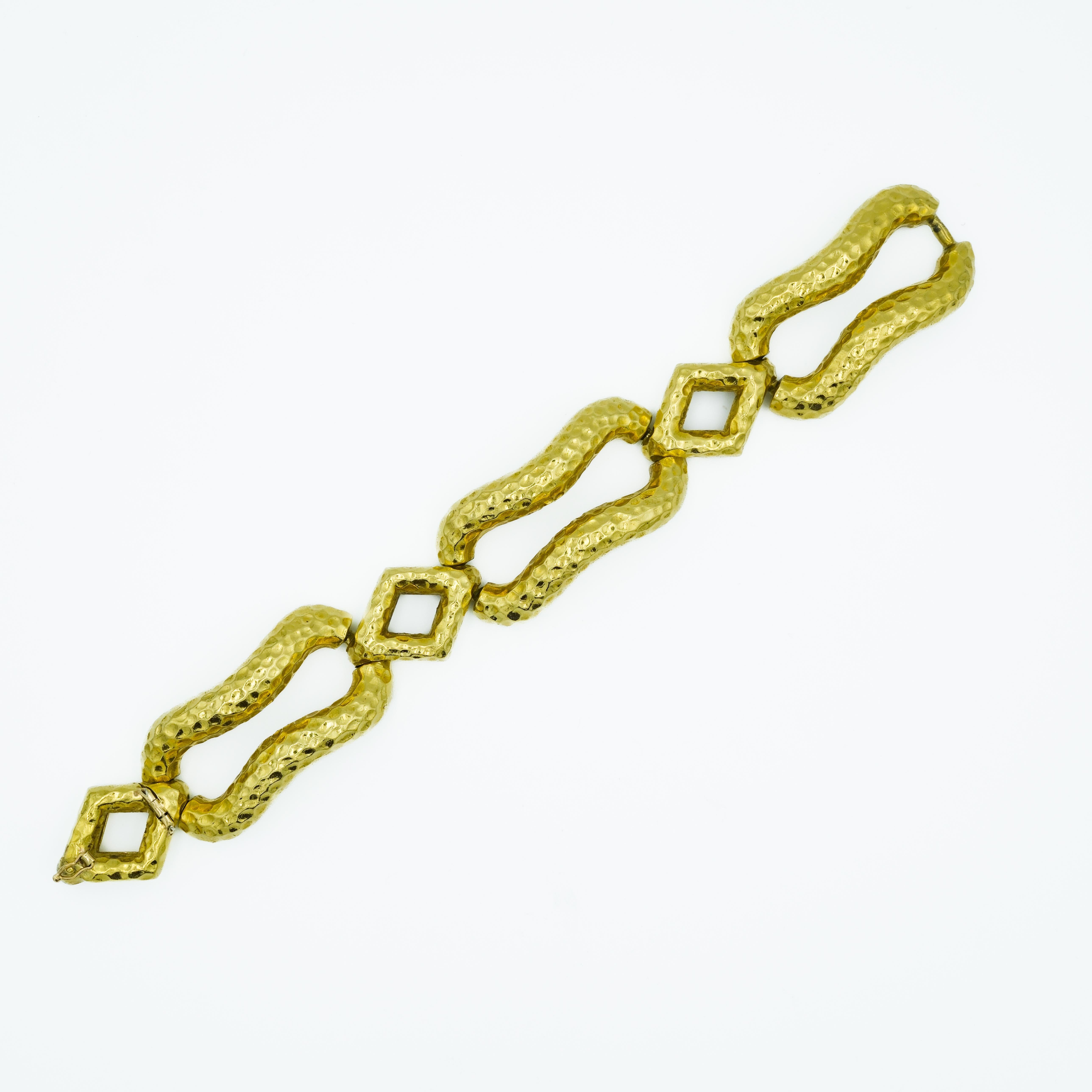 This Mid-Century modernist bracelet is crafted from 18 Karat Yellow Gold. It comprises a series of textured, hammered links. Each link presents a unique form, alternating between modified, rounded rectangular shapes and connectors, creating a bold,